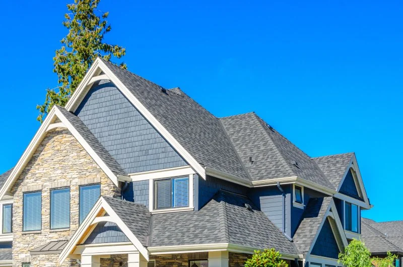House with gray roof, blue siding, and stone accents against clear blue sky.