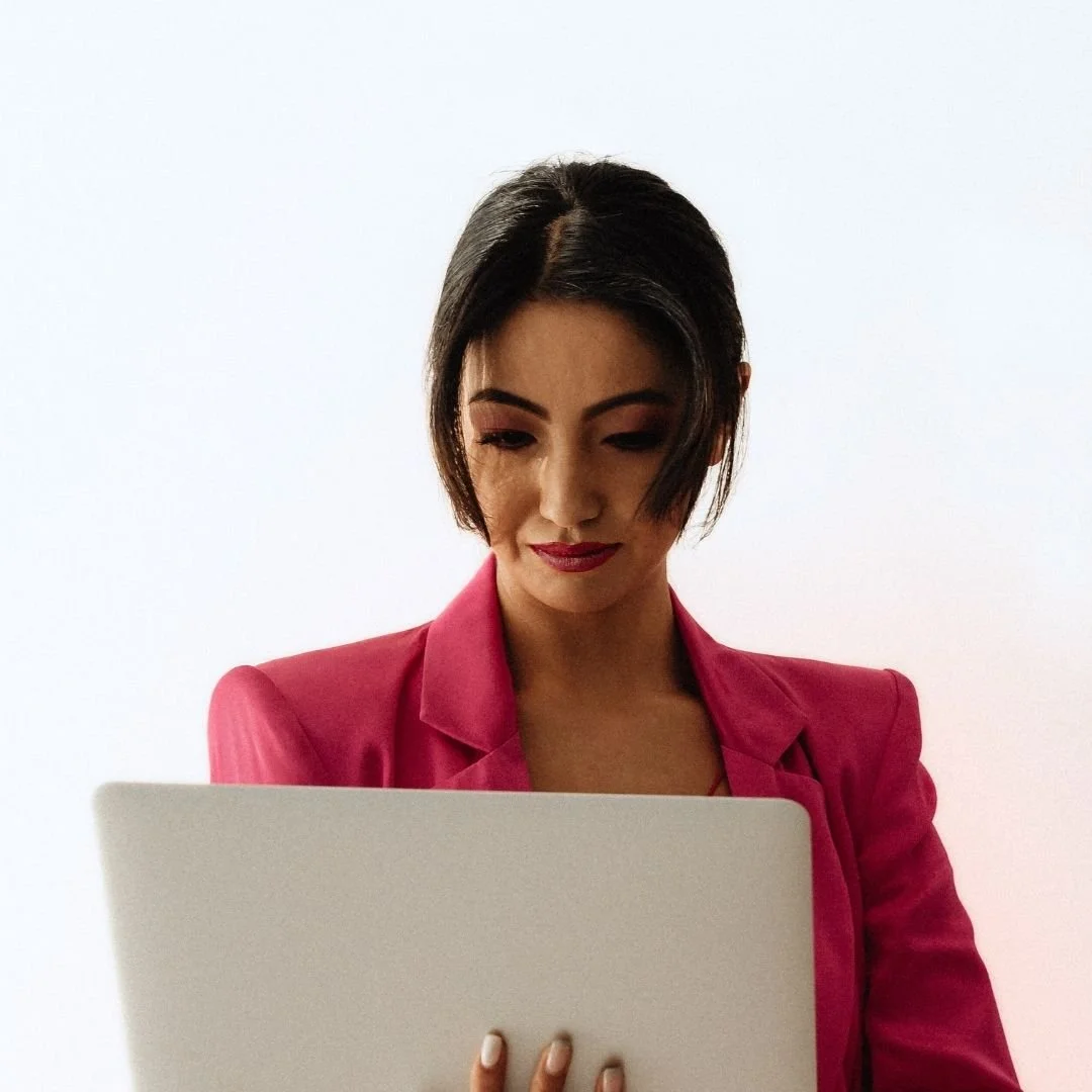 Woman with short black hair, wearing a pink blazer, looking at a tablet.