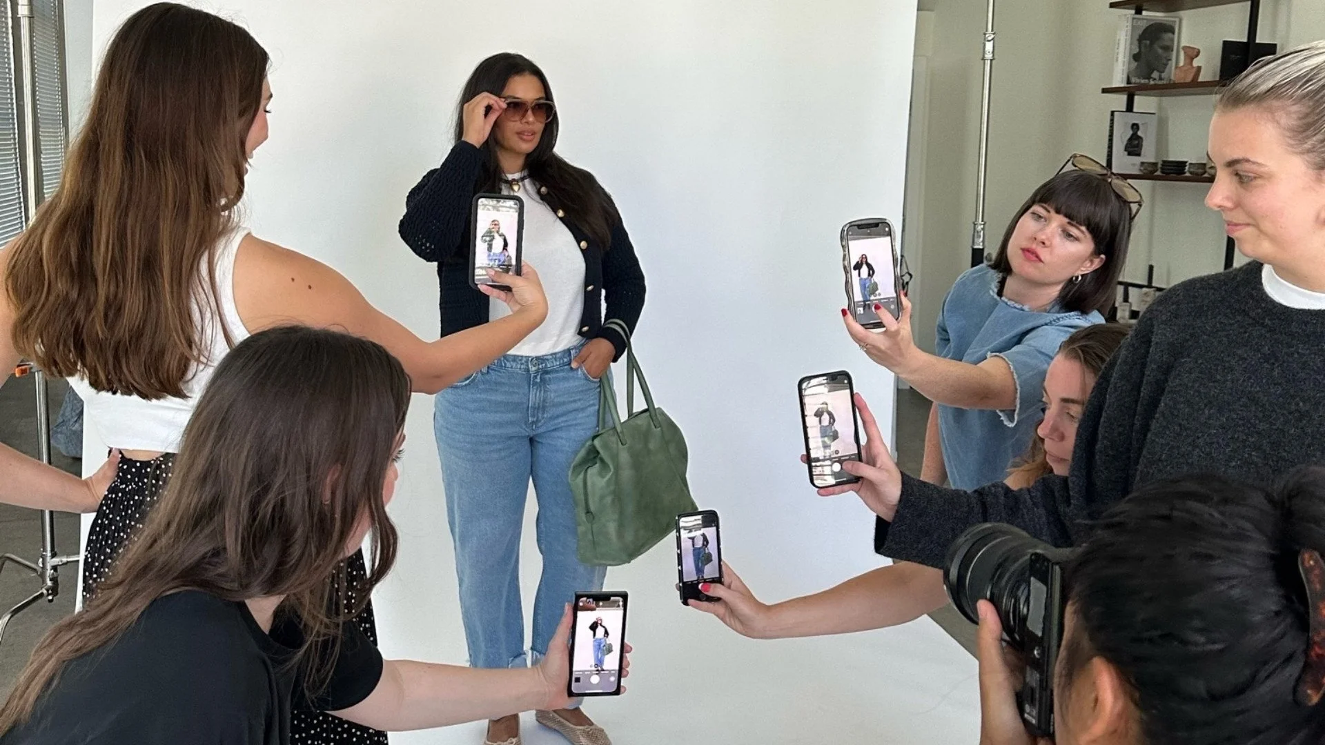 A woman posing confidently while others around her take photos and videos with smartphones in a photography studio.