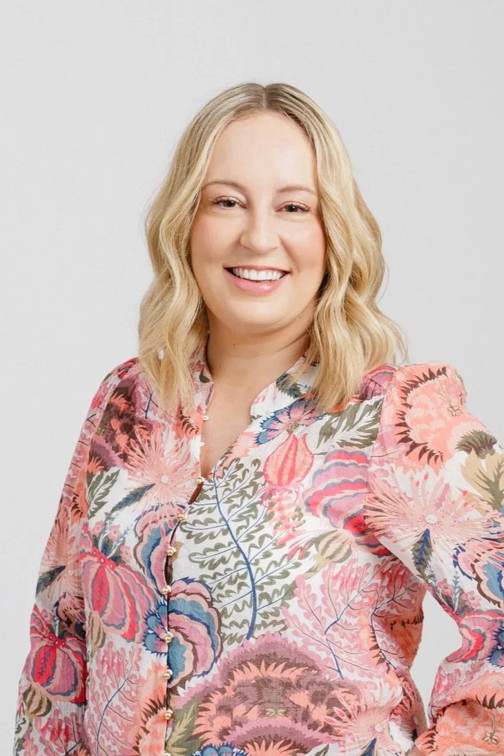 headshot of a blonde woman in a pink patterned shirt in front of white background