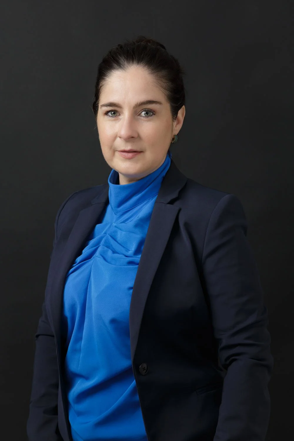 female lawyer in navy blazer and blue blouse with hair pulled back on black background