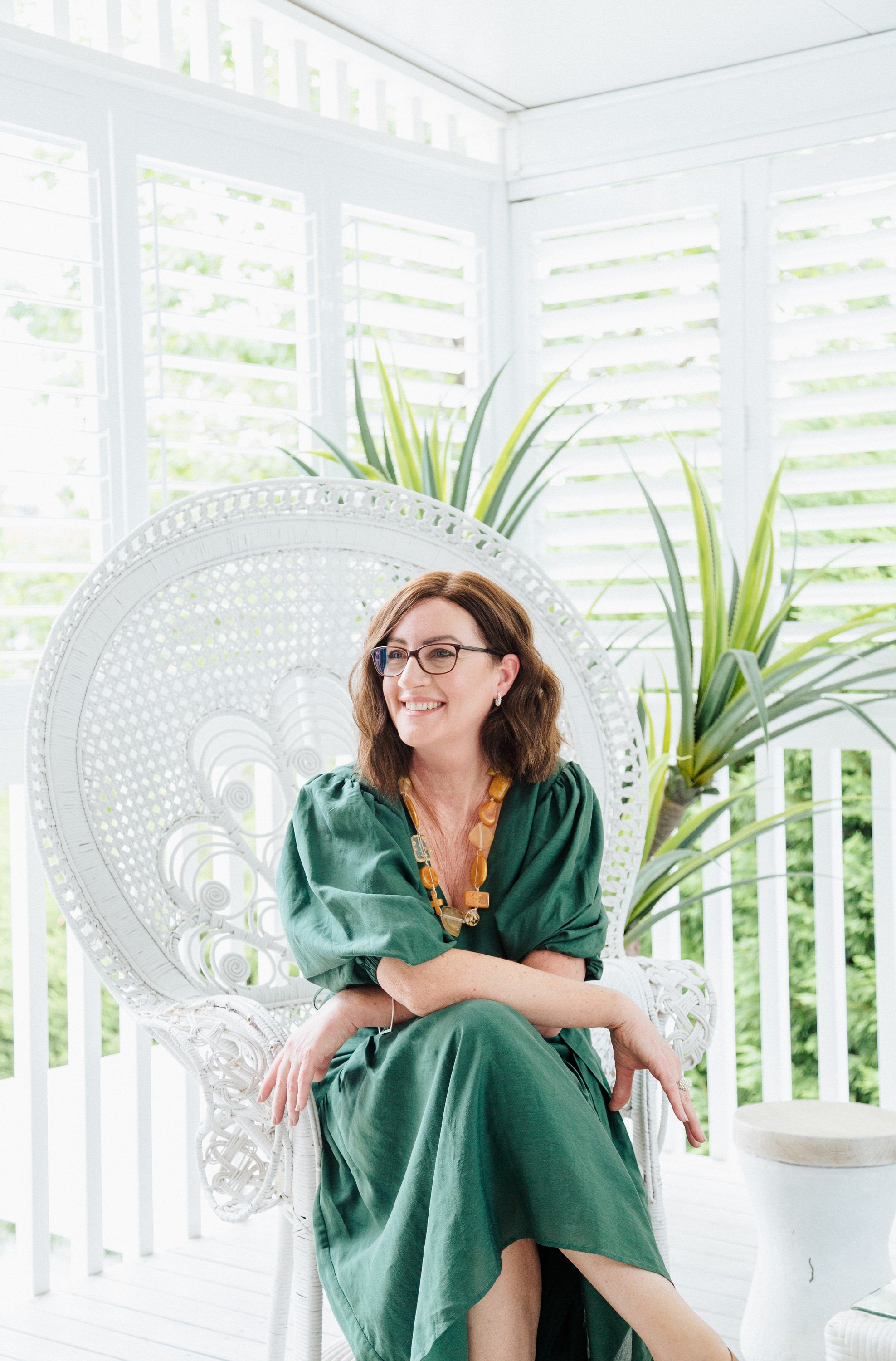 woman in green dress sitting in a white wicker peacock chair