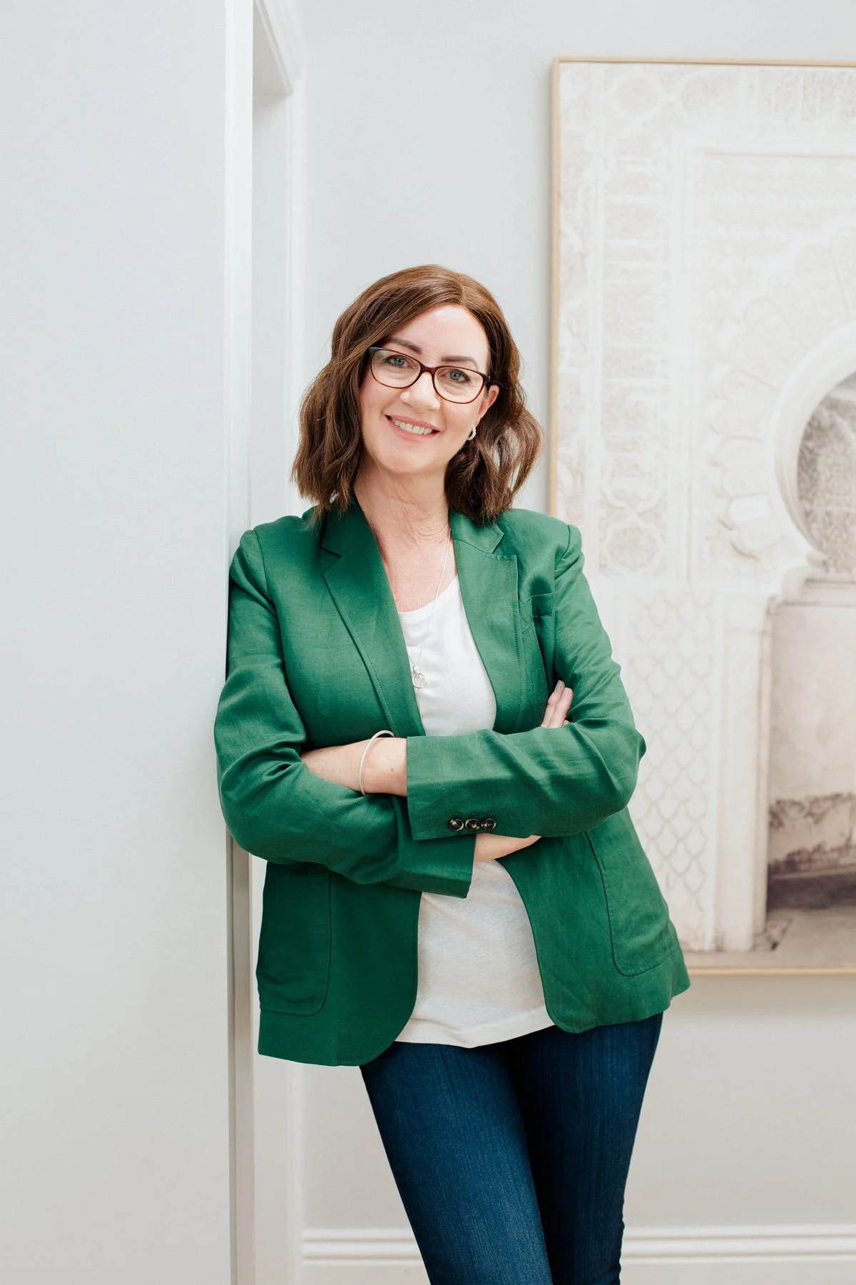 woman in green blazer leaning against a grey wall