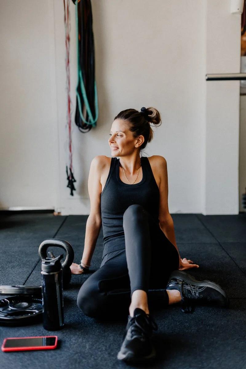 female personal trainer sitting on the floor of her home gym in black singlet and leggings