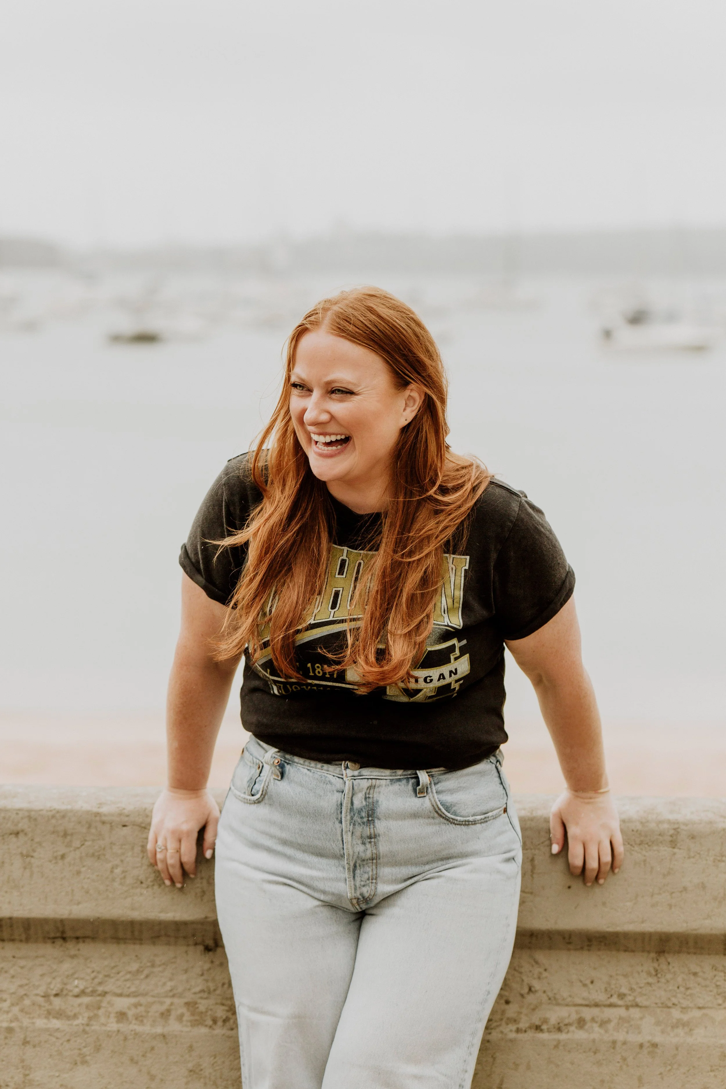 red haired young woman laughing wearing a black tee and light coloured jeans