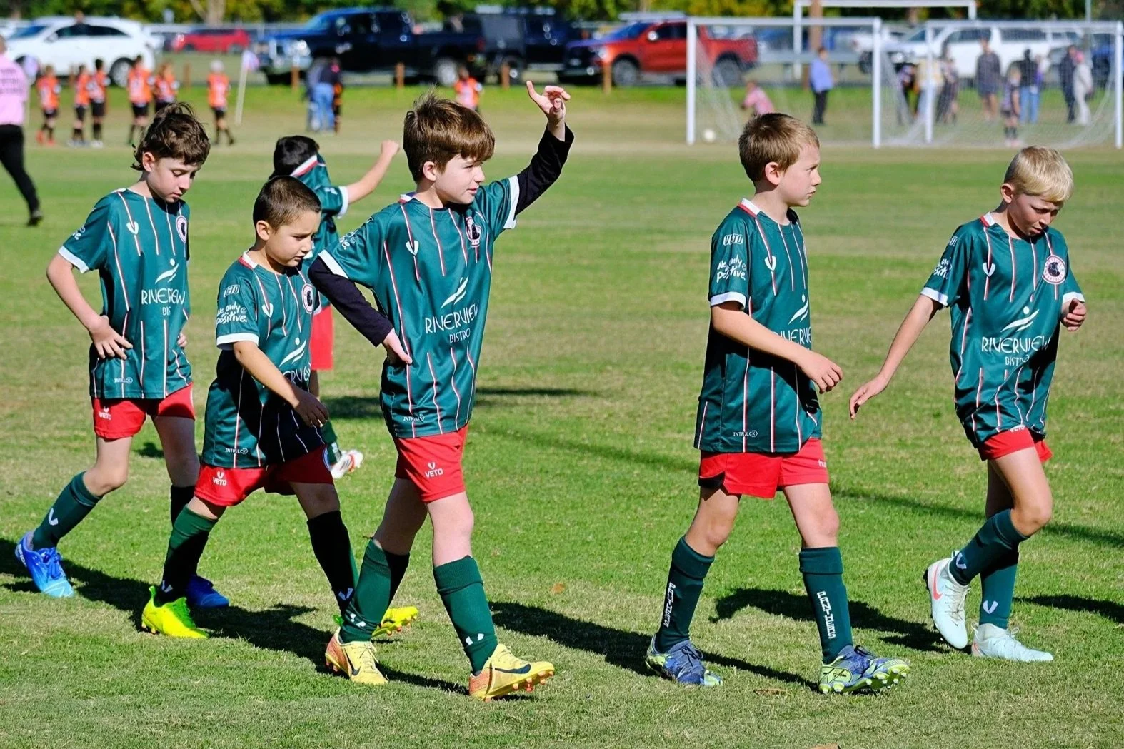 Young boys in soccer uniforms walking on a grassy field, with some holding hands and others walking separately, during a youth soccer game.