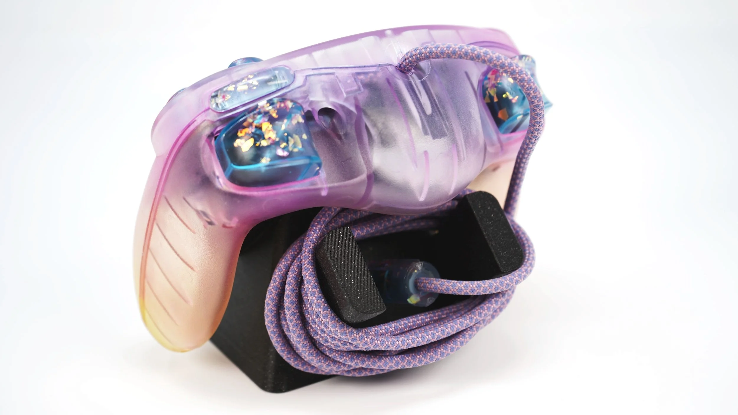 Close-up of a colorful VR headset with a purple and pink strap, resting on a black stand, with a purple and black braided cable
