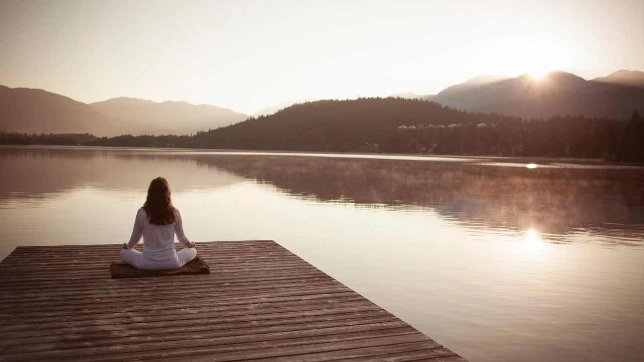 Frau die am Wasser sitzt und meditiert