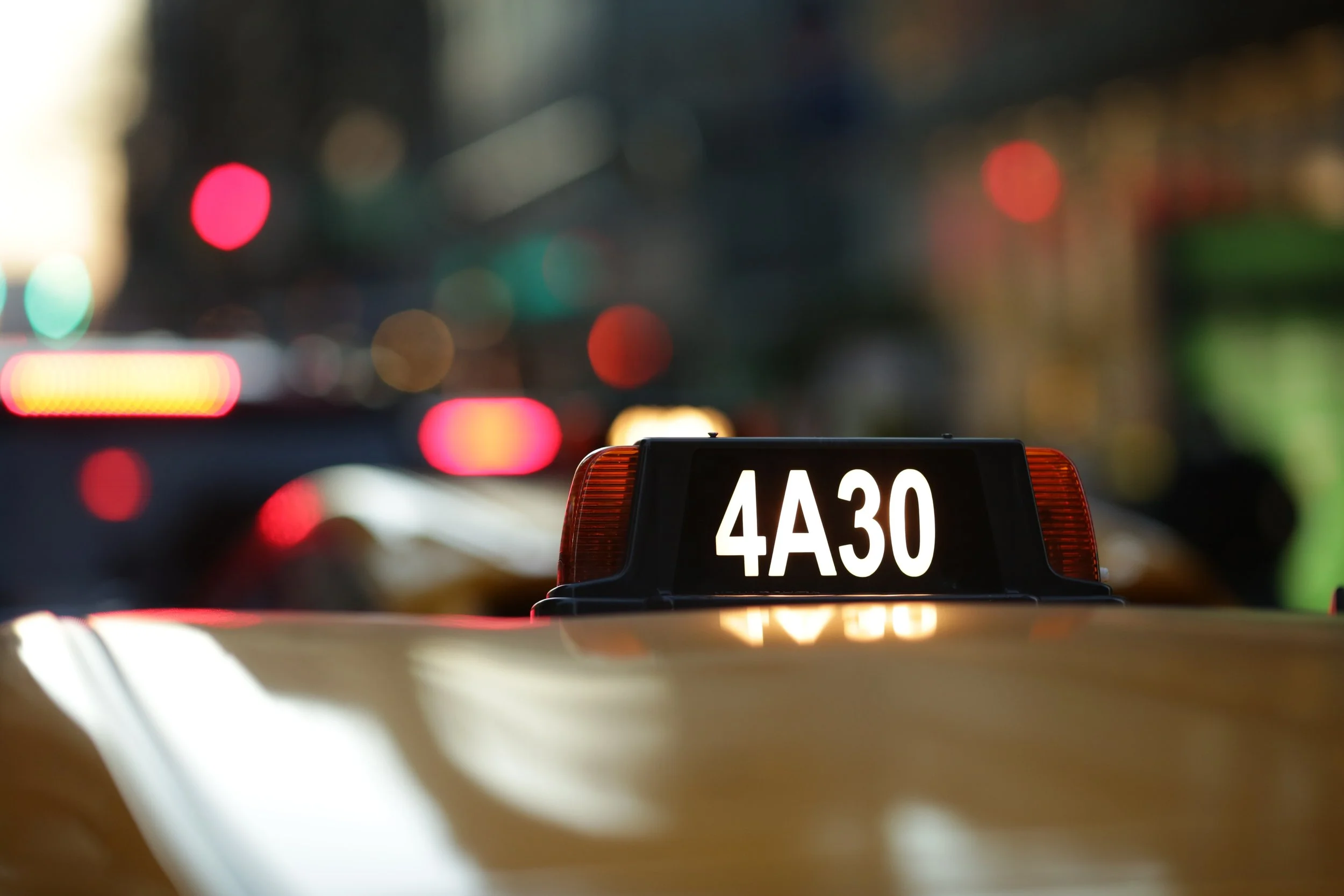 Close-up of a taxi top sign showing the number 4A30 with blurred city lights in the background.