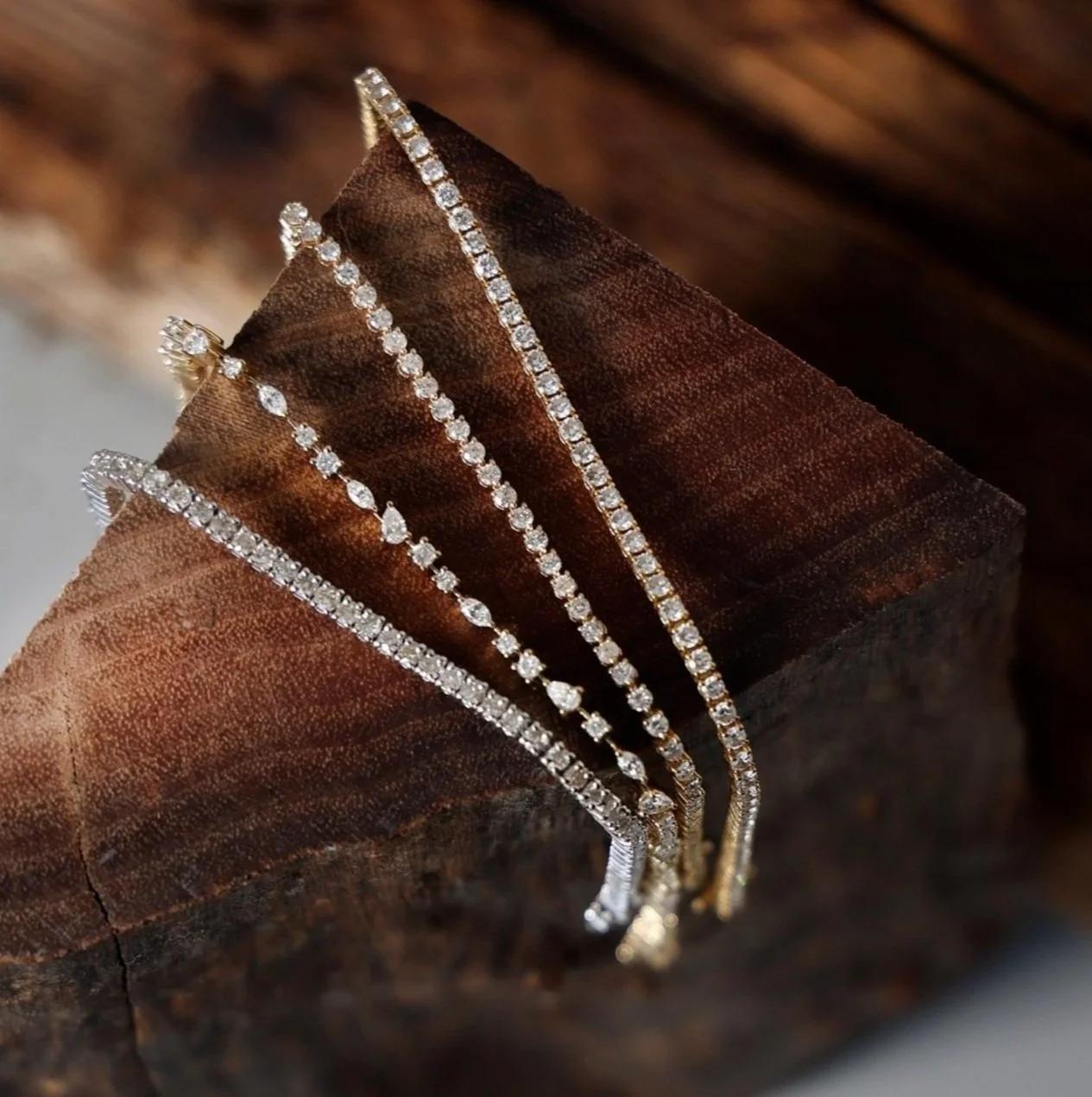 4 diamond and gold tennis bracelets displayed on a piece of wood