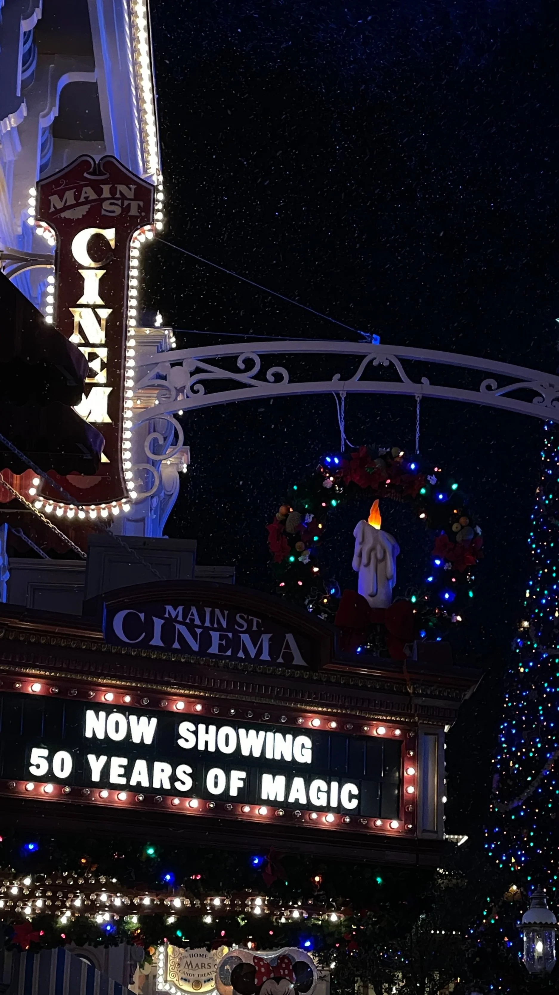 Movie theater marquee at night celebrating 50 years of magic, decorated with Christmas wreaths and lights, showing 'Now Showing 50 Years of Magic'.