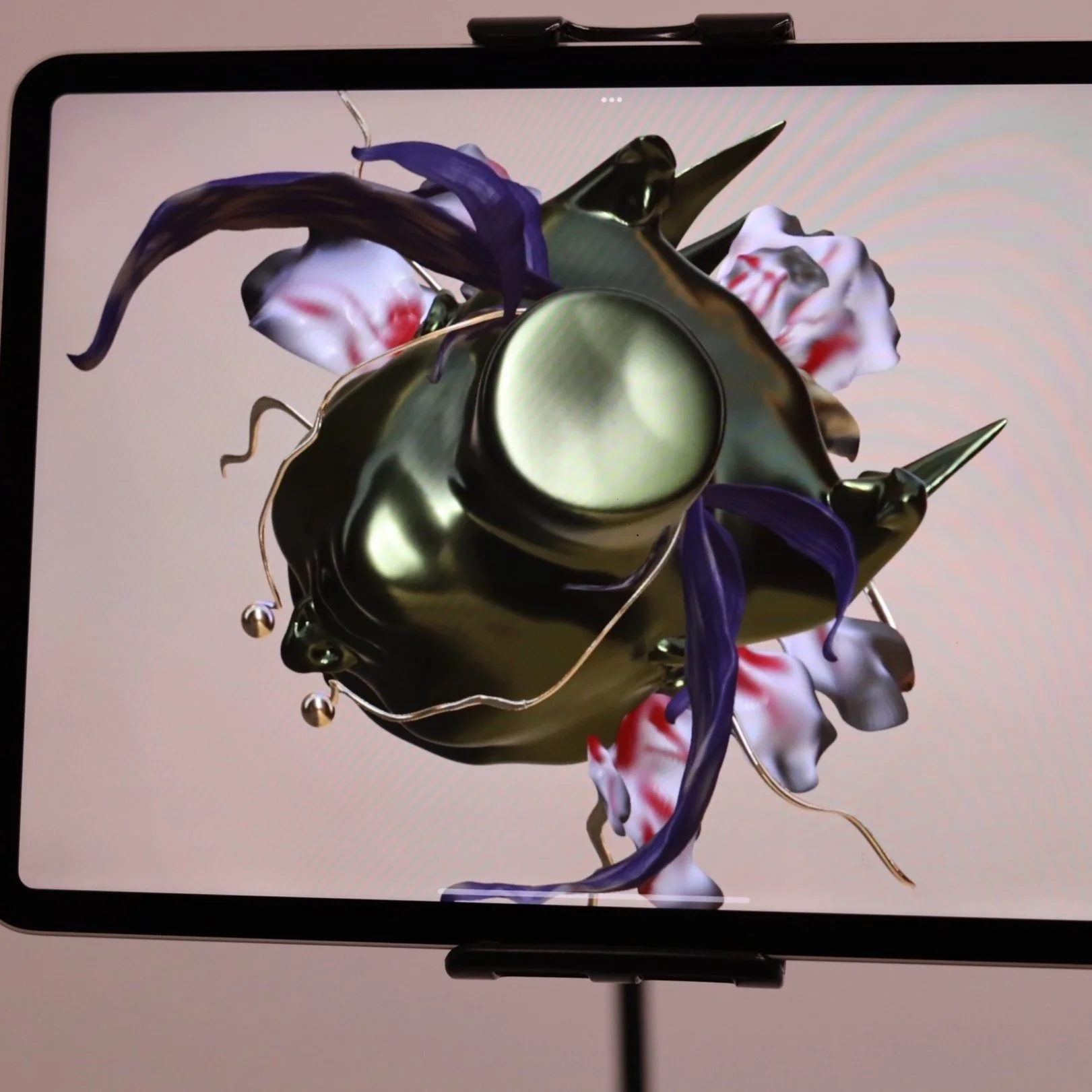 Close-up of a digital screen displaying a 3D model of an abstract, shiny, metallic object with floral and organic elements, including purple and white flowers.