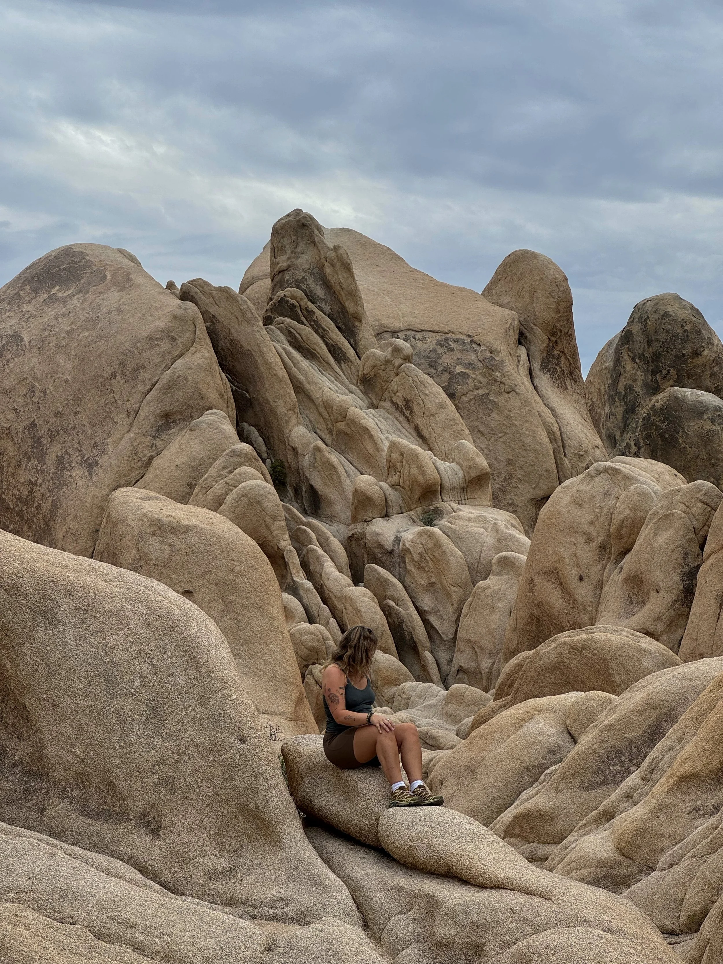 Maddie sitting on a boulder among giant granite rock formations under a cloudy sky