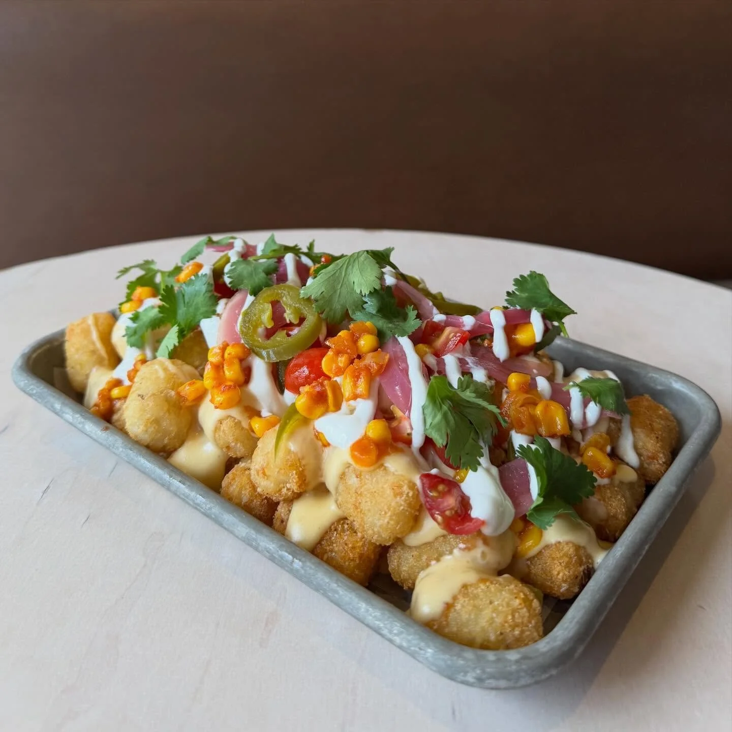 TATER-TOCHOS 
Spiced tater tots, warm queso, tomato, jalape&ntilde;o, pickled onion, corn chili, crema, cilantro
