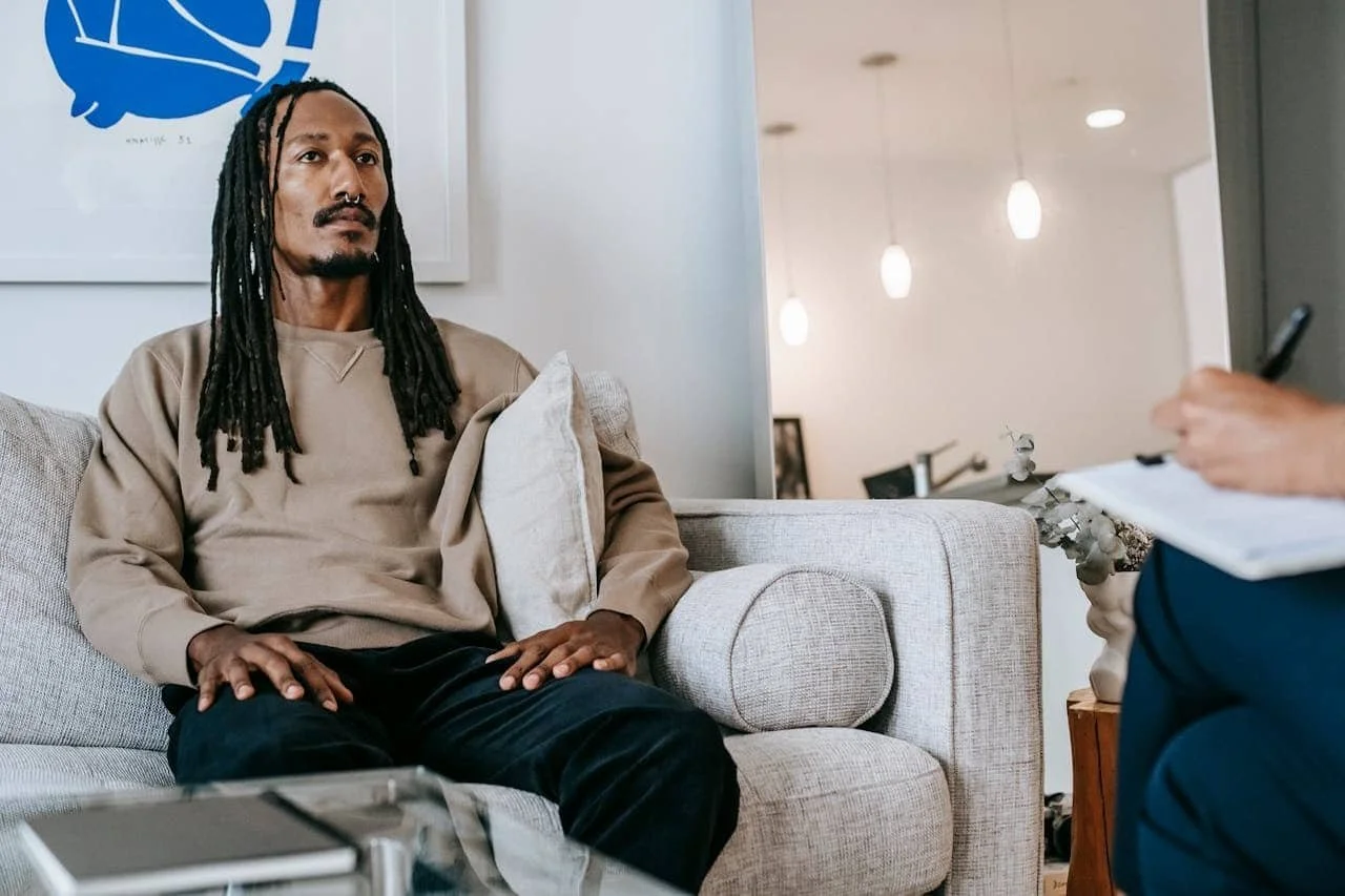 man with long dark hair sitting on a couch