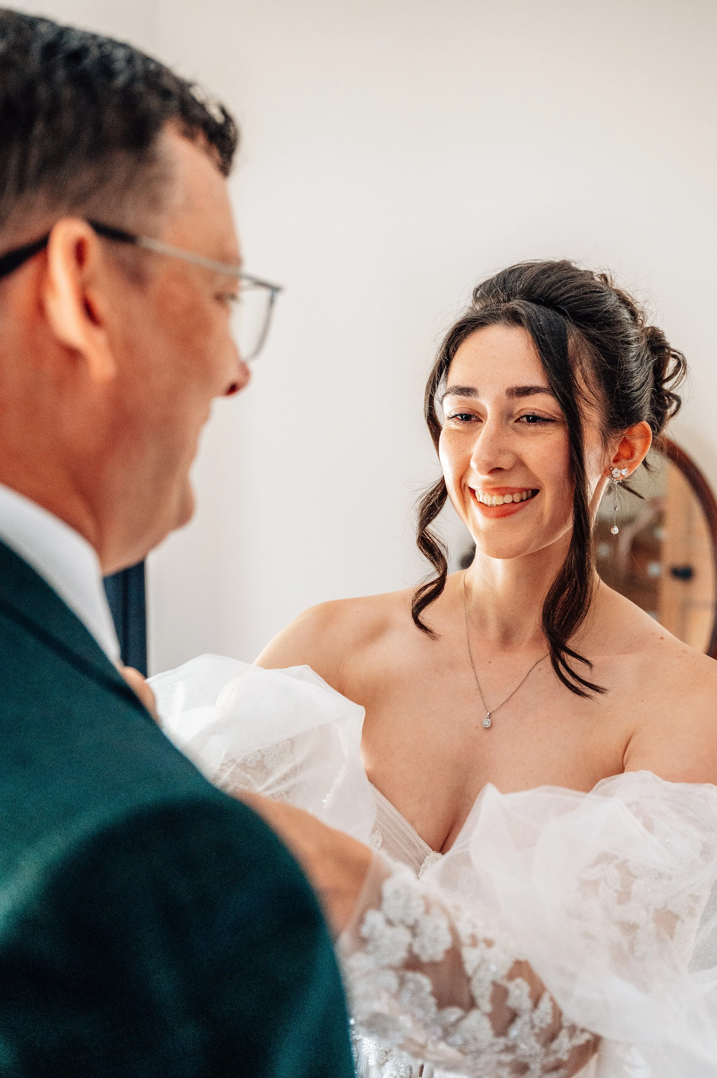 A bride smiling as her father helps her with her wedding dress.