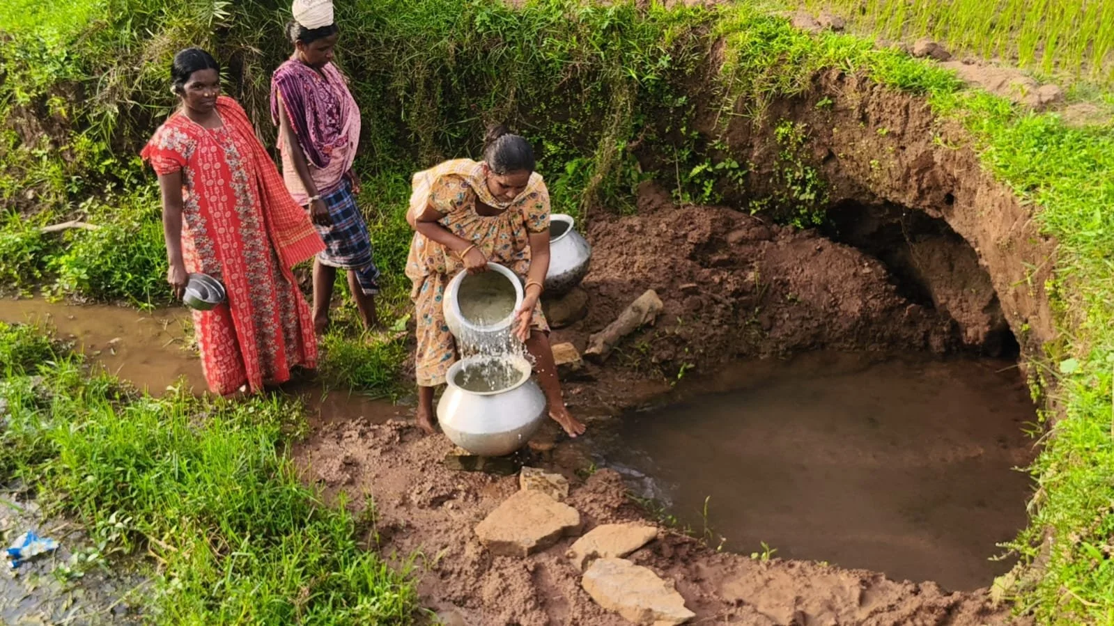 Women dipping dirty water from a muddy creek.