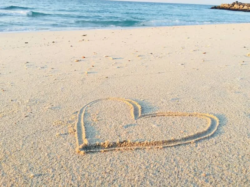 A heart drawn in the sand next to water