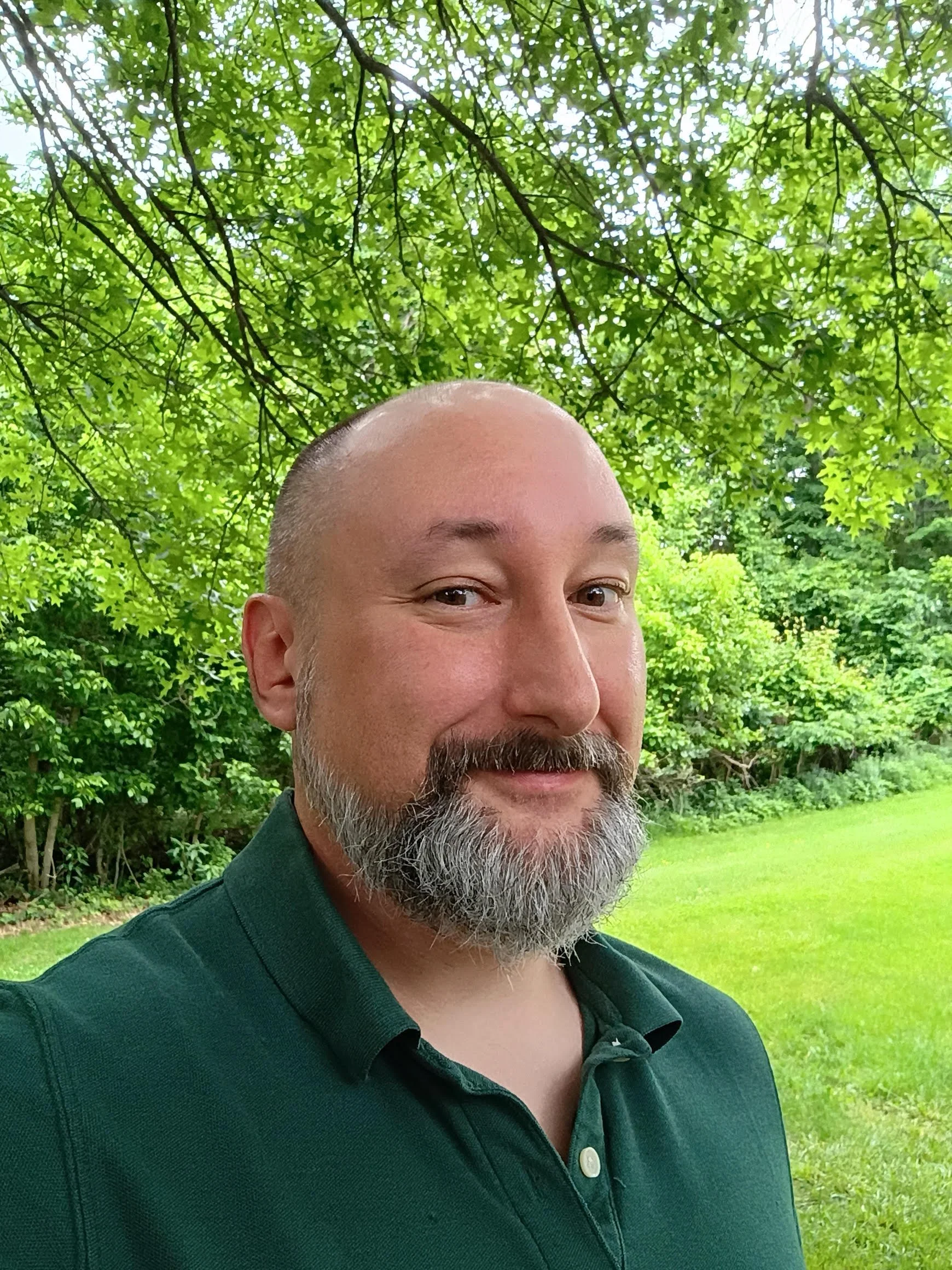 Jason standing under a tree with green shrubbery behind