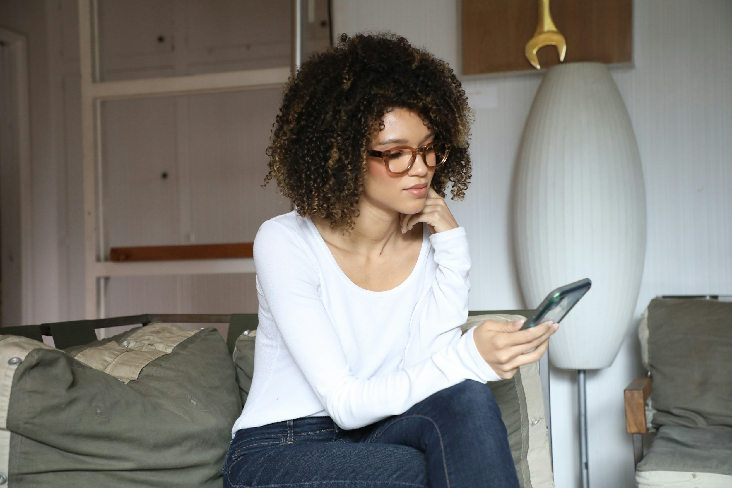 A woman sitting on a couch scrolling on her phone, symbolizing the emotional pressure and comparison many moms feel from parenting content online.