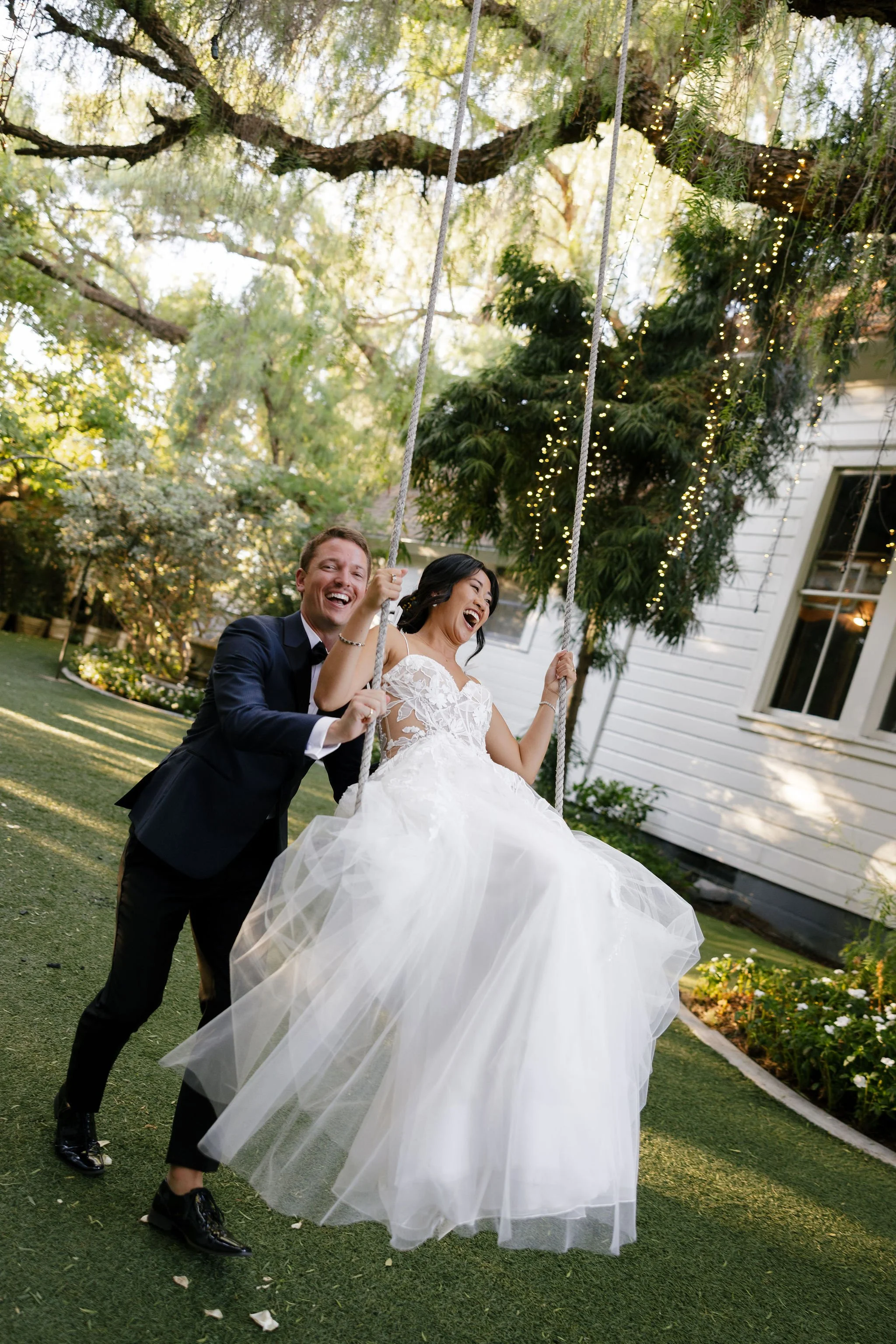 Groom pushing bride on swing, laughing, having fun at wedding