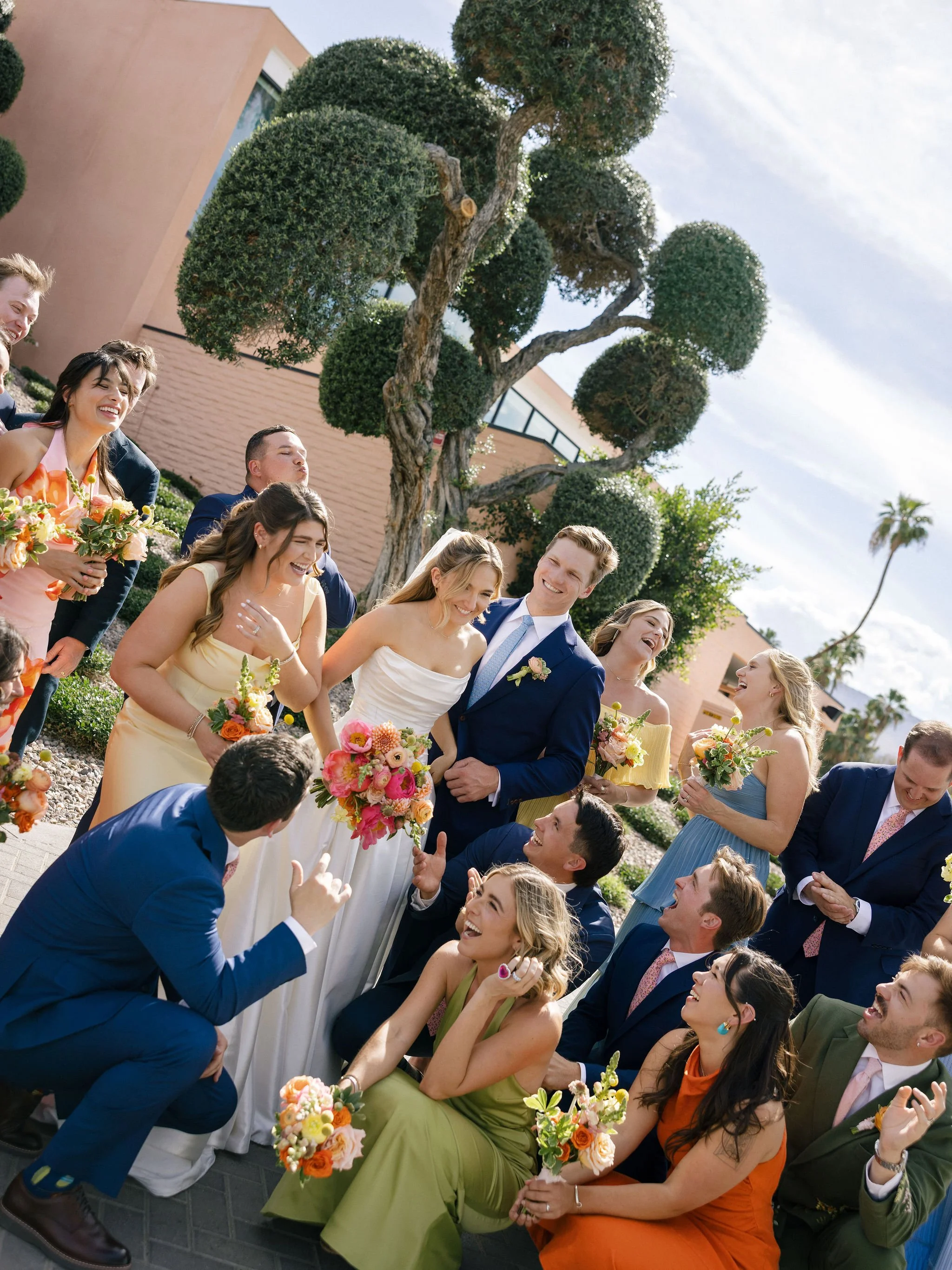 colorful wedding party laughing together with a pink background in Palm Springs