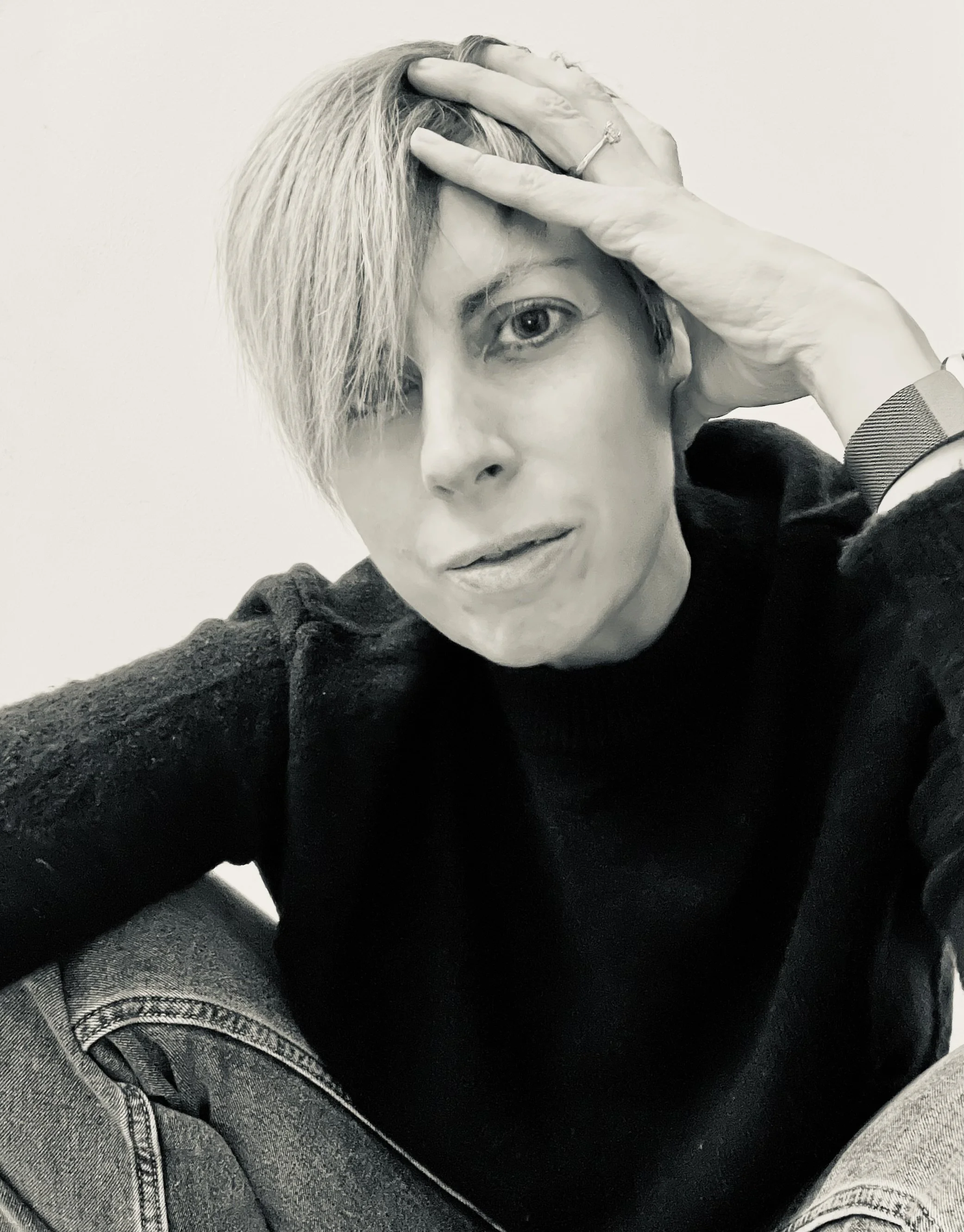 Valeria Brigatti in black and white, wearing a black sweater and denim jeans, with short hair covering one eye.