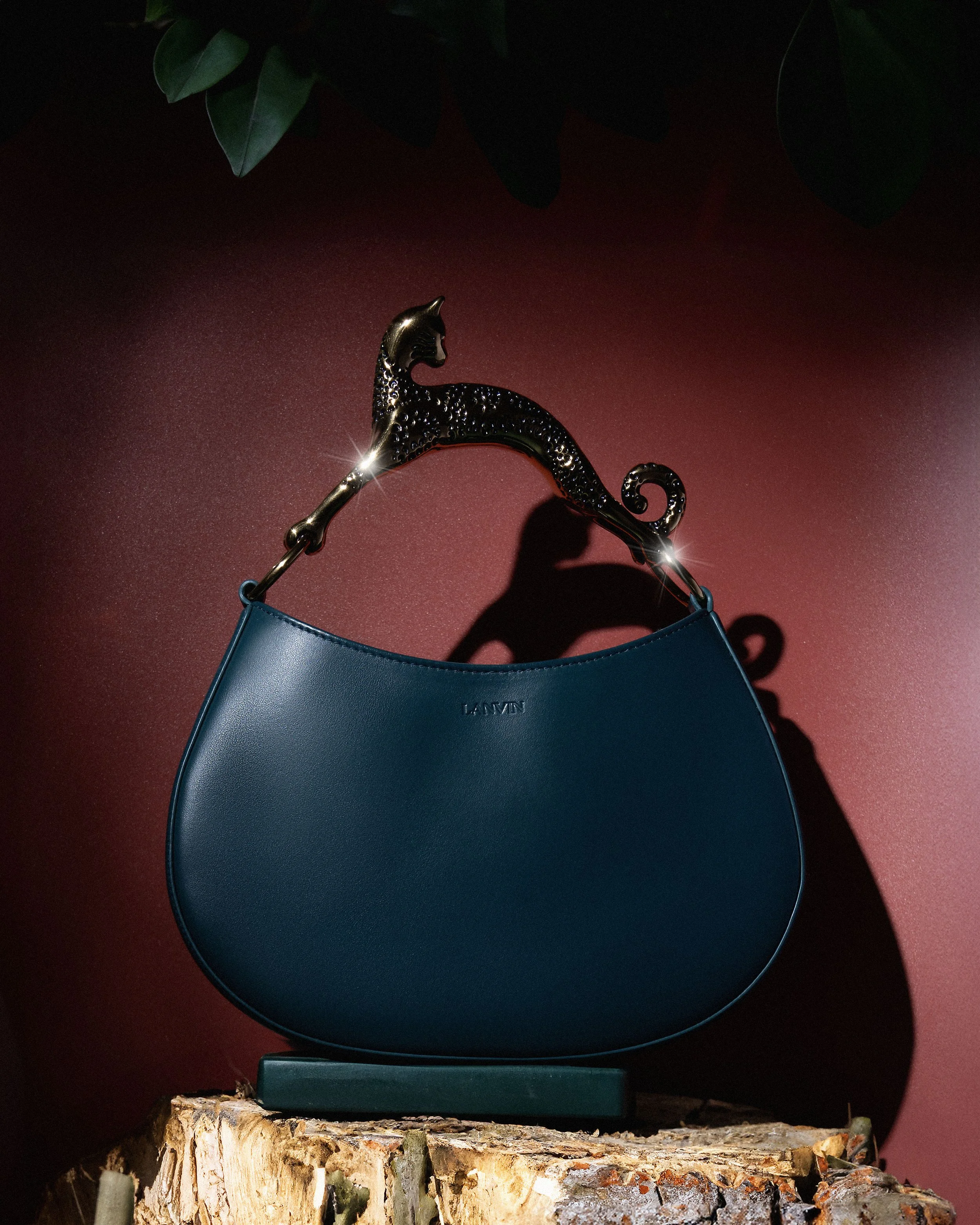 A blue handbag with a leopard-shaped handle resting on a tree stump against a red background.