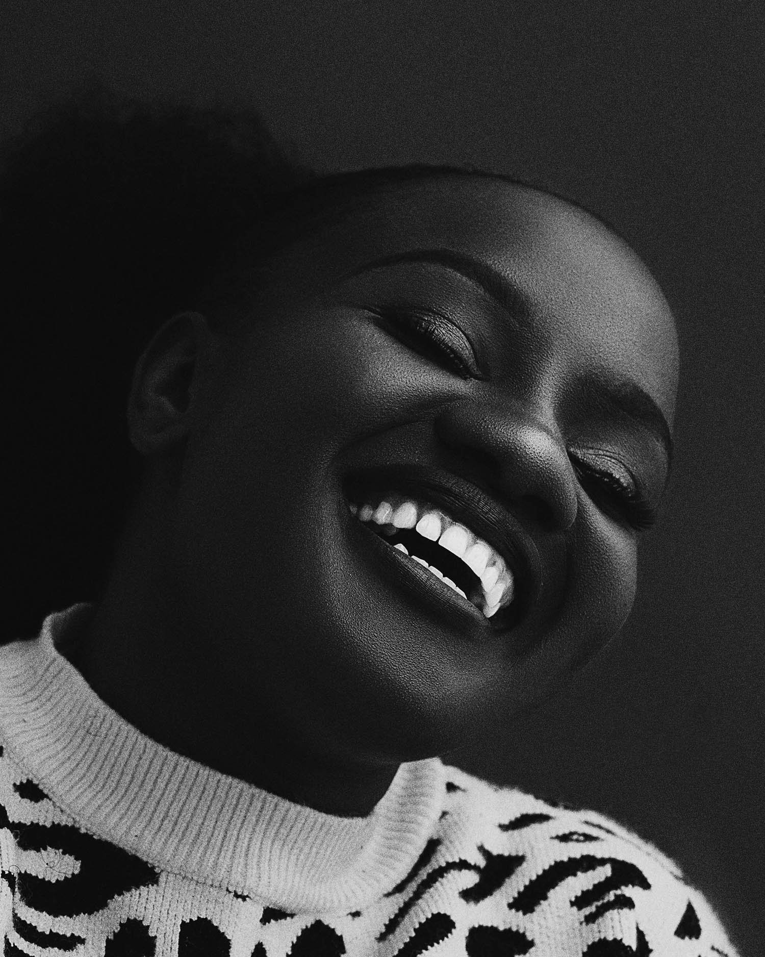 Close-up black and white photo of a woman smiling, wearing a patterned sweater.