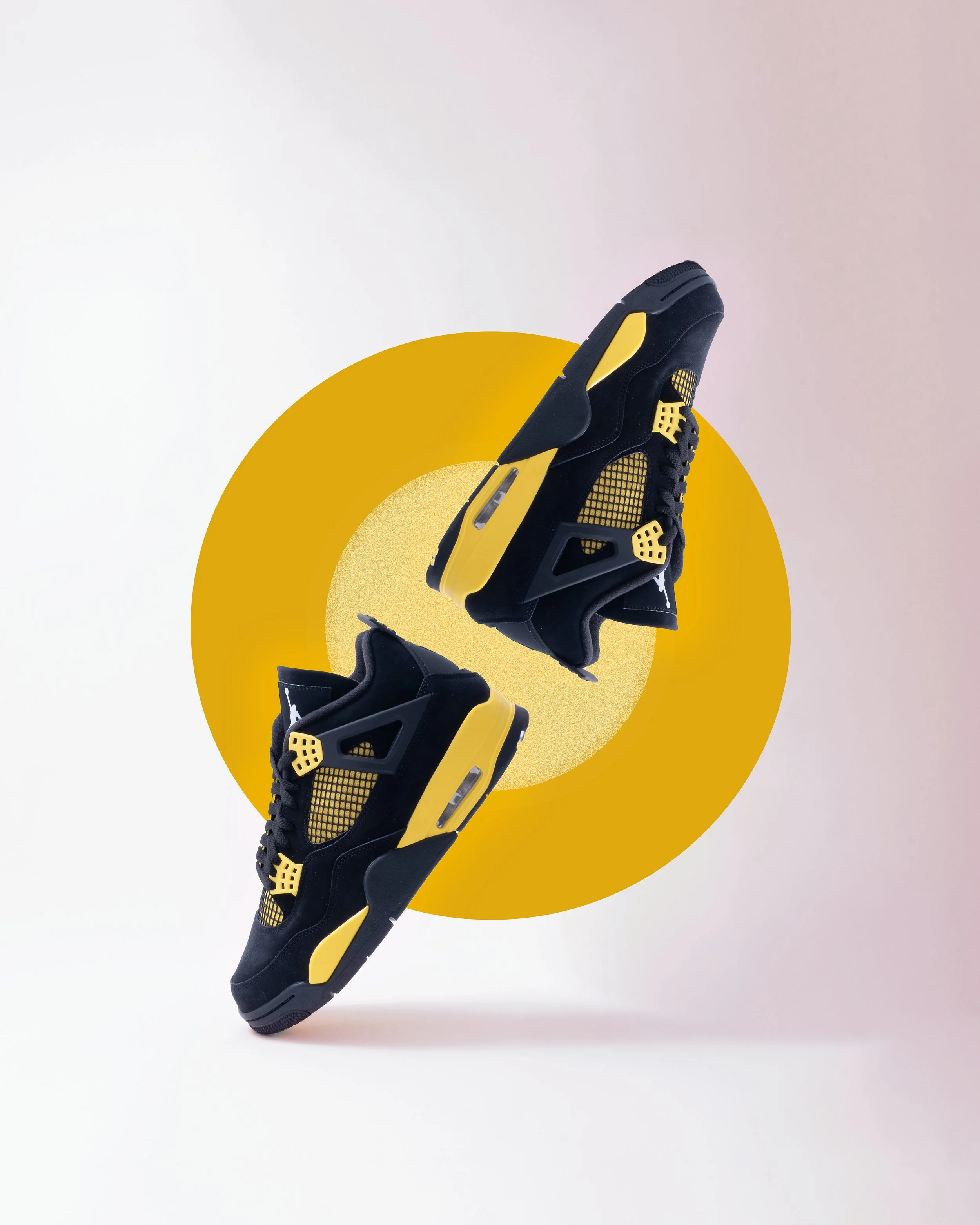 A pair of black and yellow Air Jordan sneakers floating in front of a background with a pink top and white bottom, overlaid with a yellow and beige geometric circle.