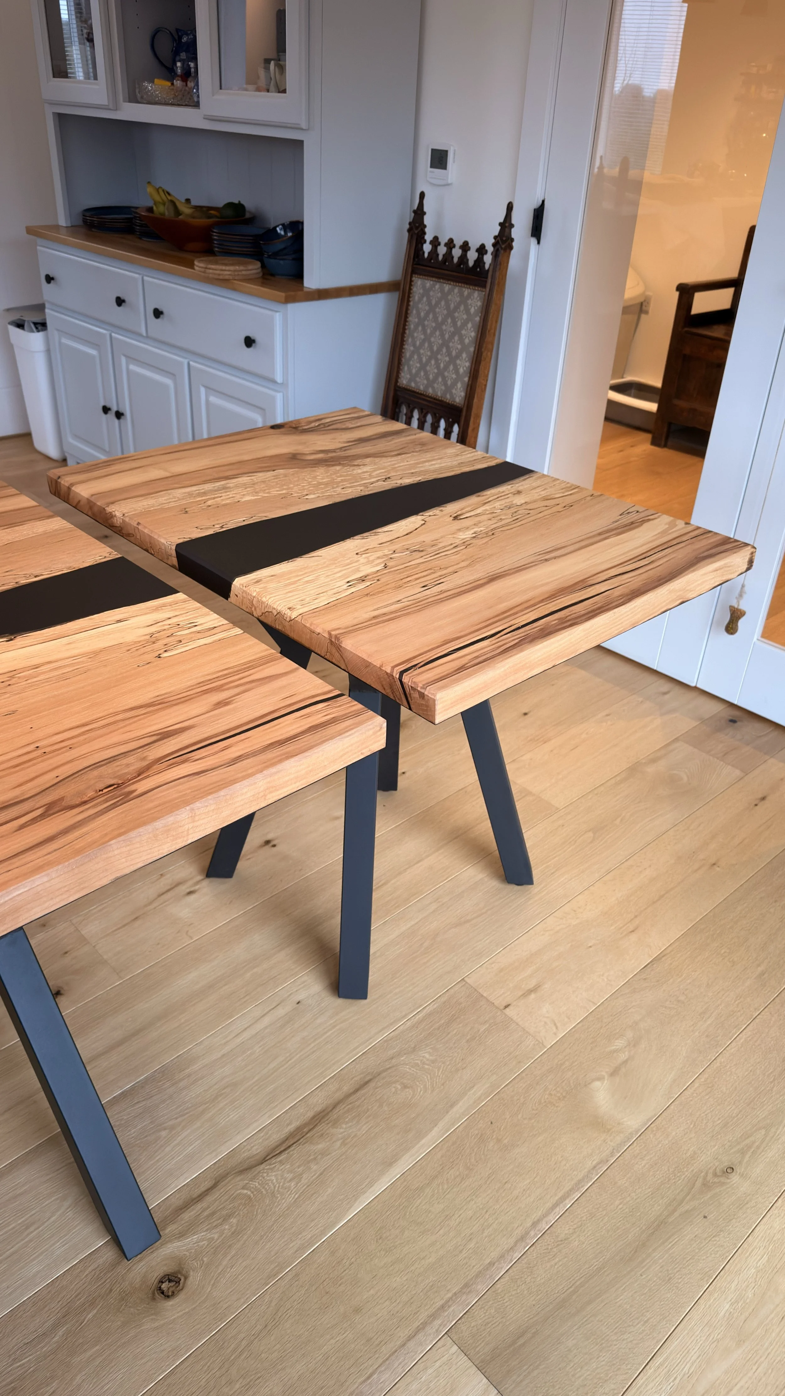 A wooden dining table with black accents and angled black legs in a kitchen or dining area.