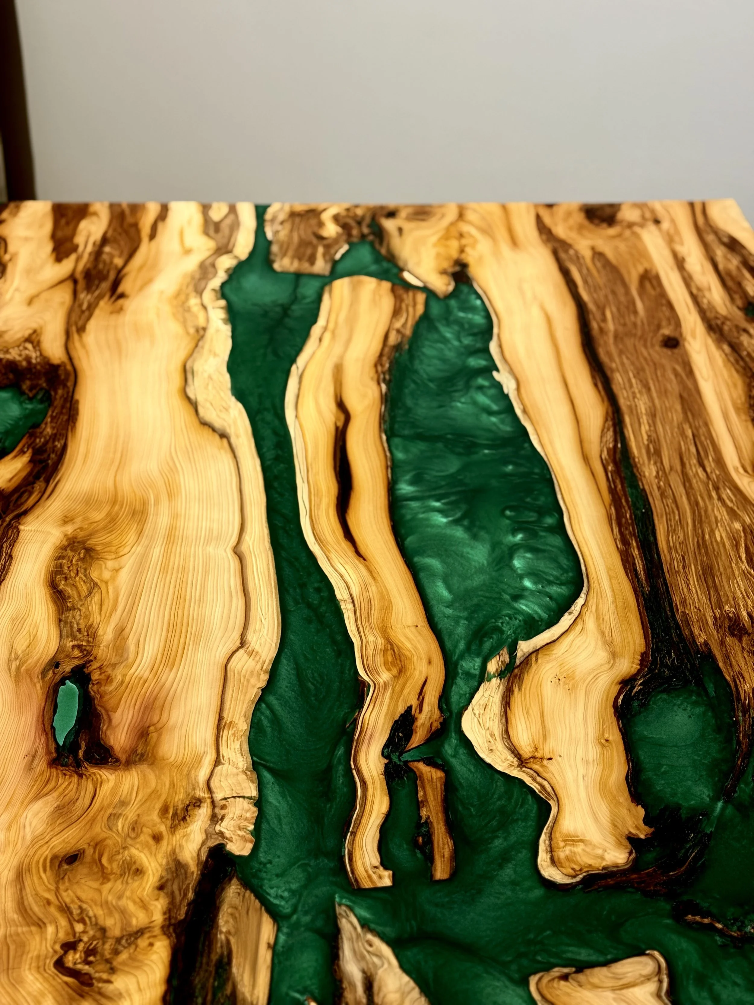 Close-up of a wooden table with natural wood grain and green resin inlays.