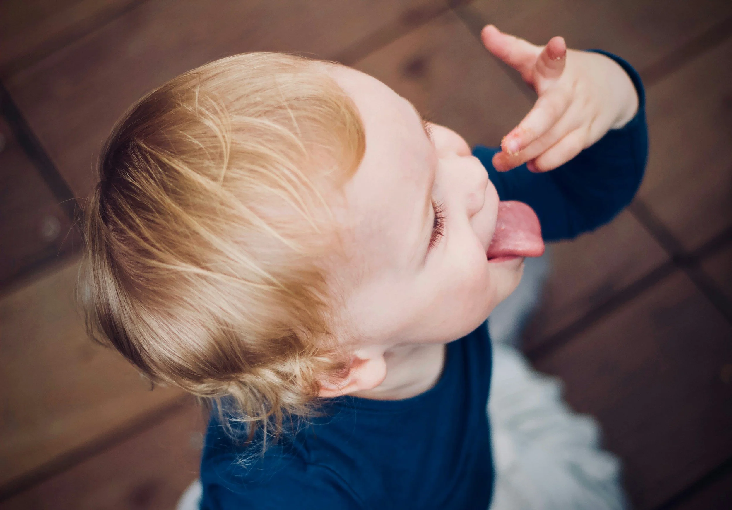 Close-up of a young child with red hair, licking their finger, and holding their hand near their face.