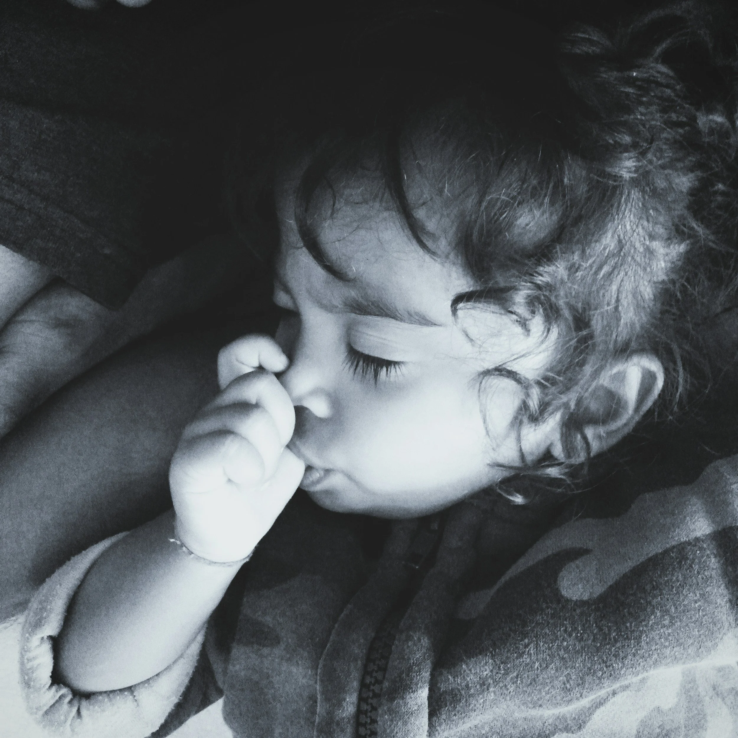 Close-up black and white photo of a young girl with curly hair, wearing gloves, holding a small object in her hand, and resting her head on her arm.
