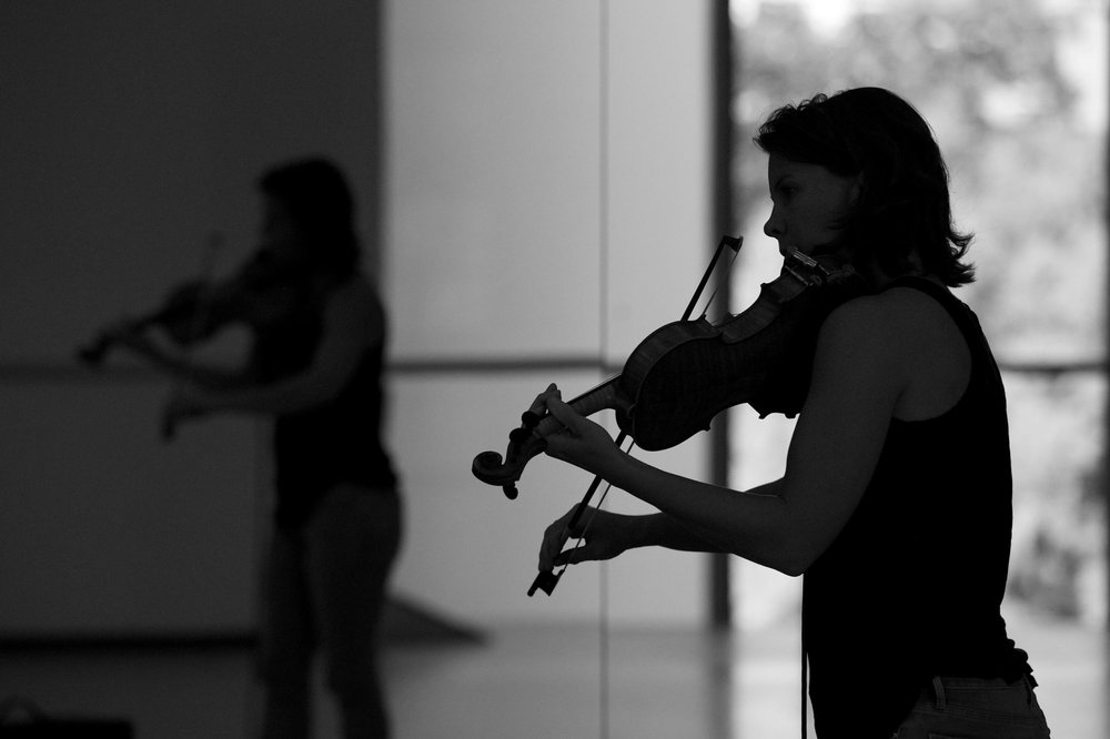  A backlit photo of Sarah Neufeld playing her violin.  