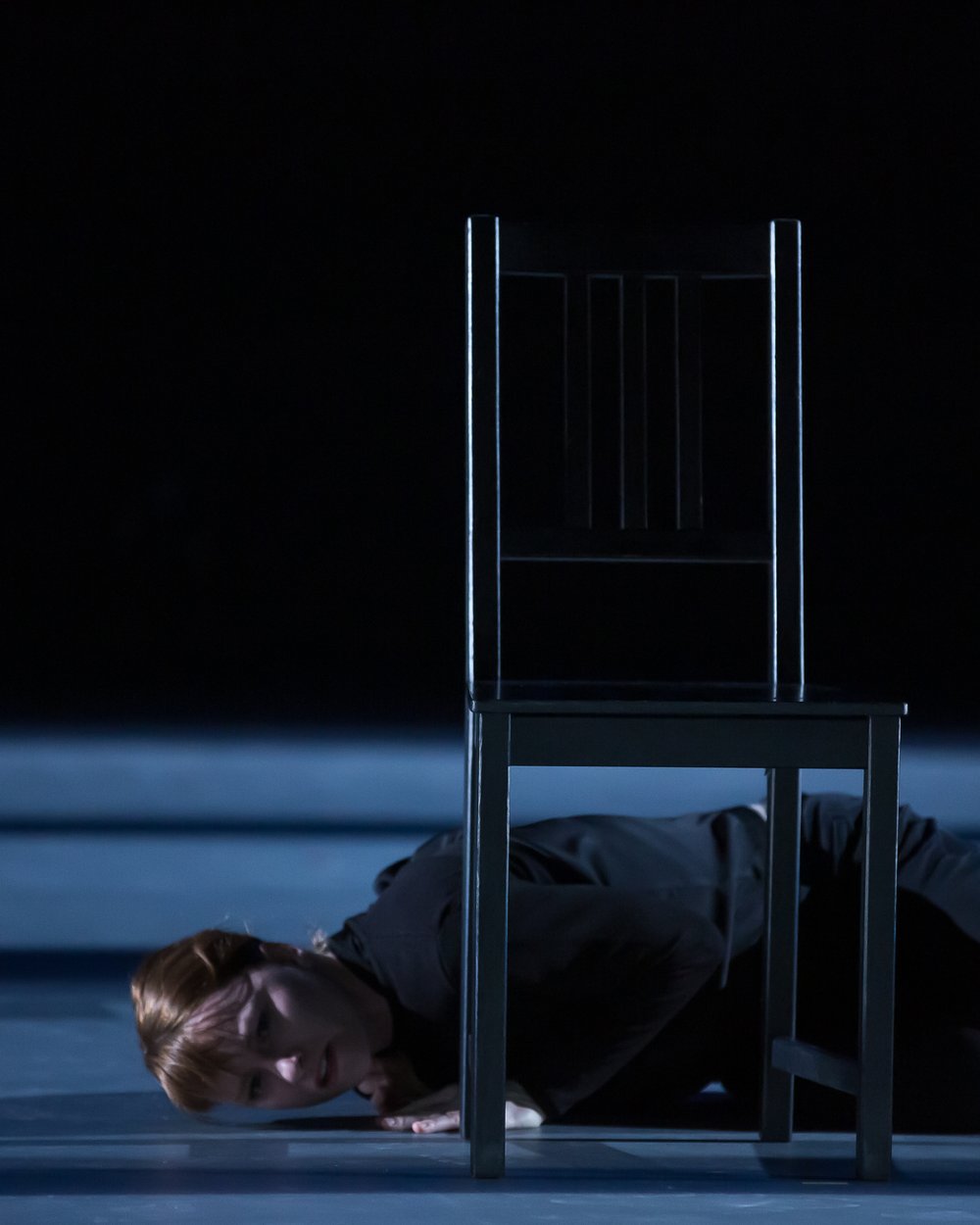  Sarah Fregeau lying on the stage, stomach down behind a chair. Her face is turned to the camera.&nbsp; 