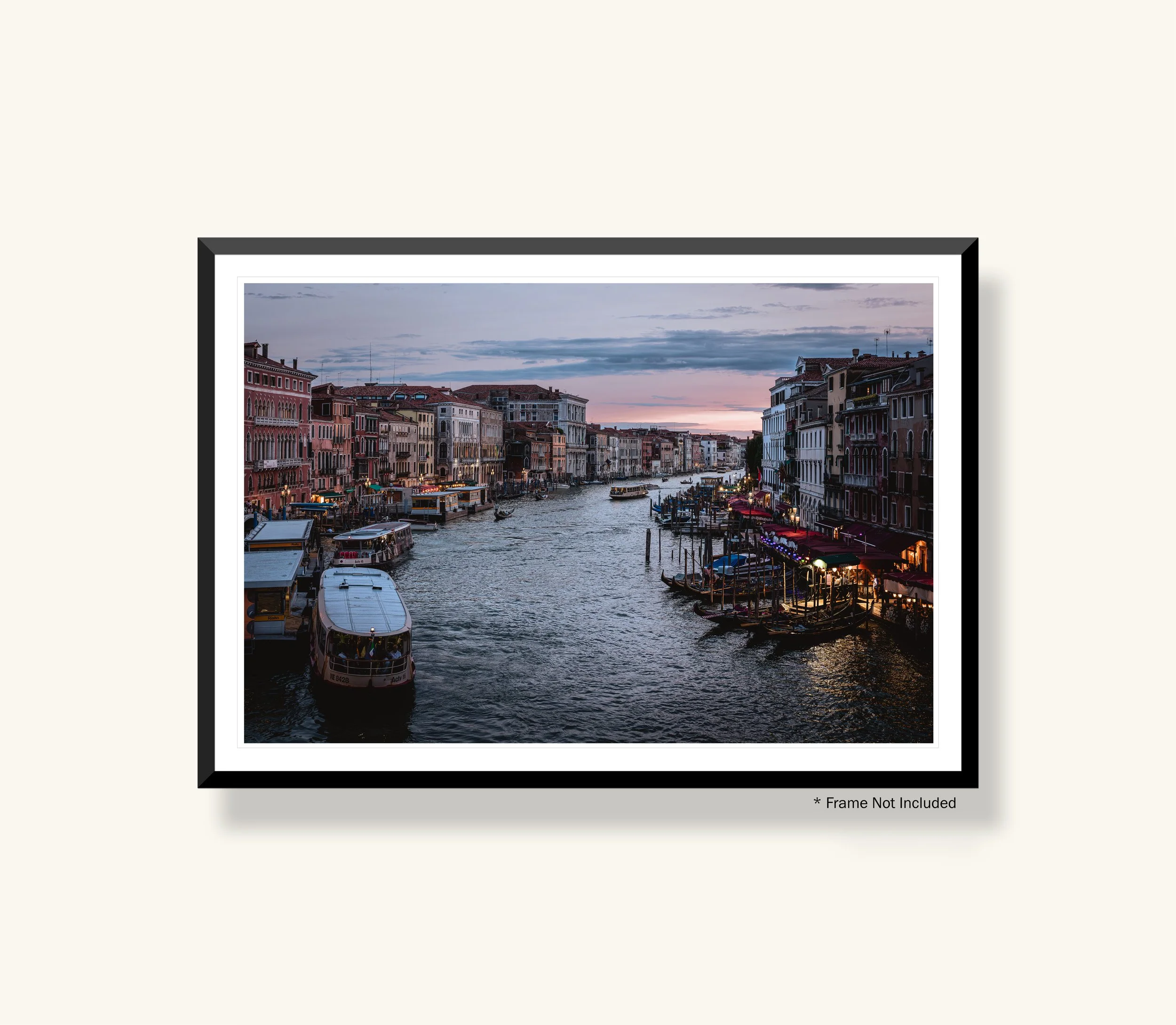 A framed photograph of a canal in Venice, Italy, with colorful historic buildings lining the waterfront and boats on the water during dusk.