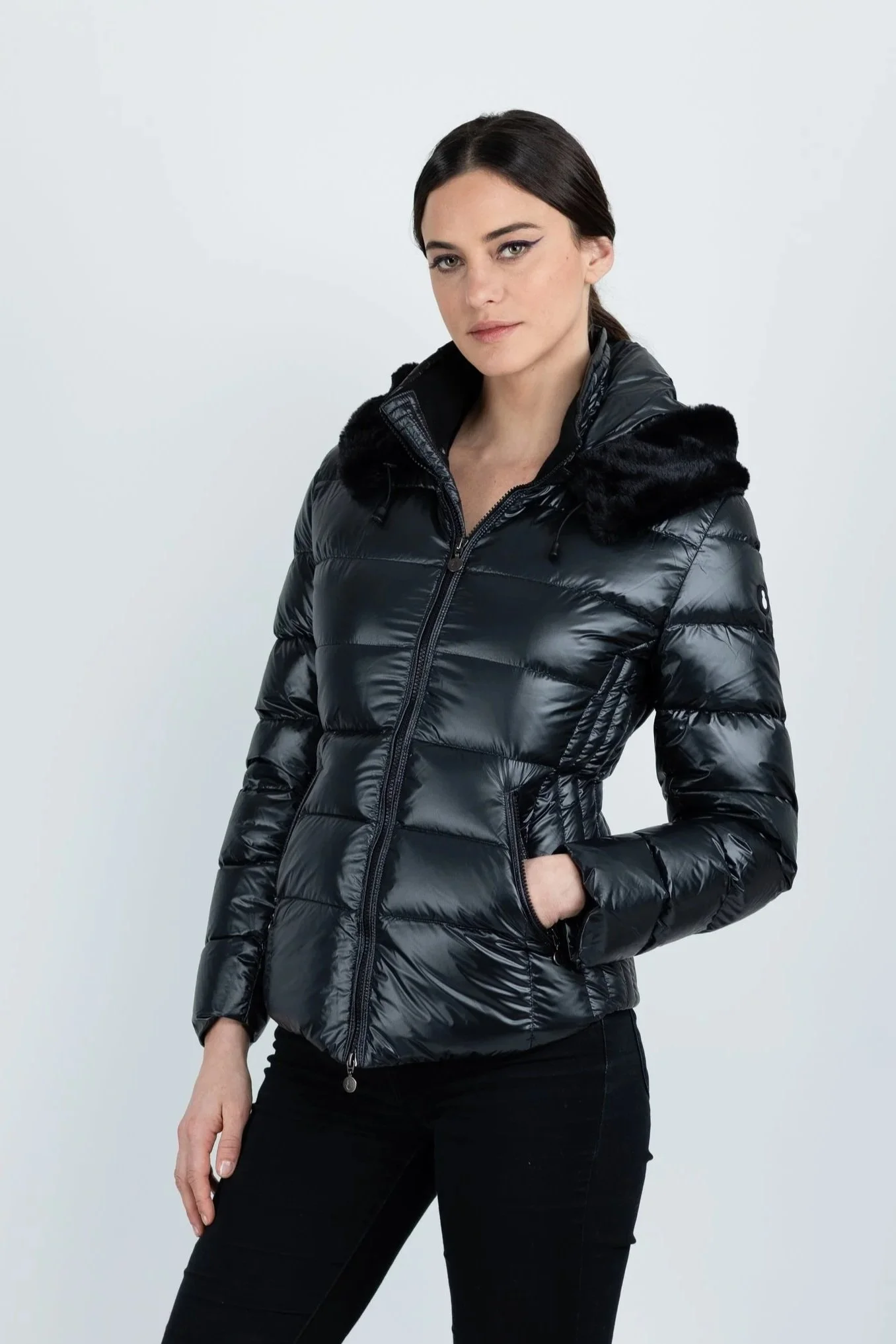 Woman wearing a black puffer jacket with a hood and black pants, posing against a plain white background.