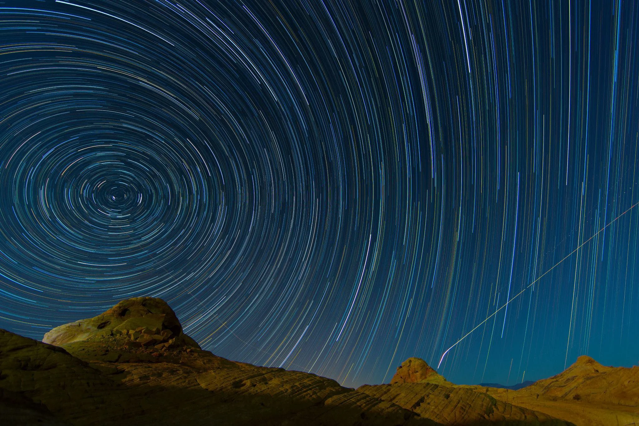 Astrophotogry photo taken in the Valley of Fire north of Las Vegas depicting star trails over rock formations with airplane trails visible on the bottom right side of the photo