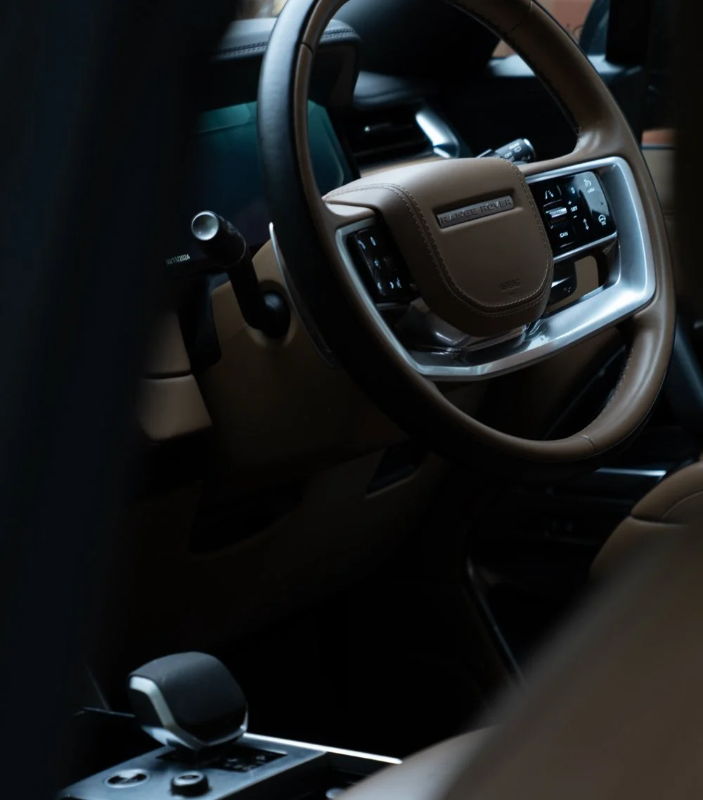 Close-up of a Range Rover vehicle interior with tan leather steering wheel and dashboard controls.