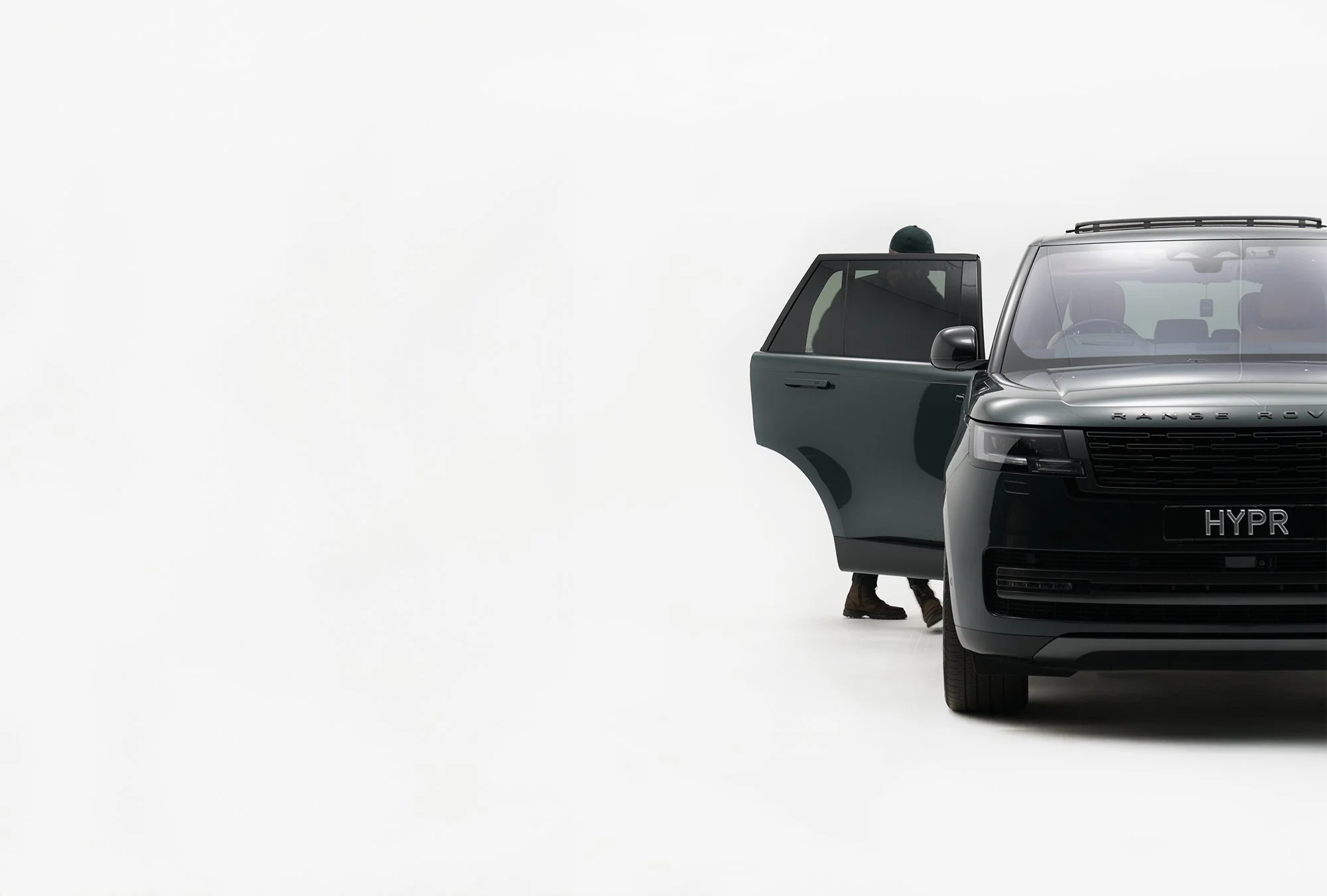 A black Range Rover with an open driver-side door, seen from the front right, with a person partially visible standing behind it in a white studio setting.