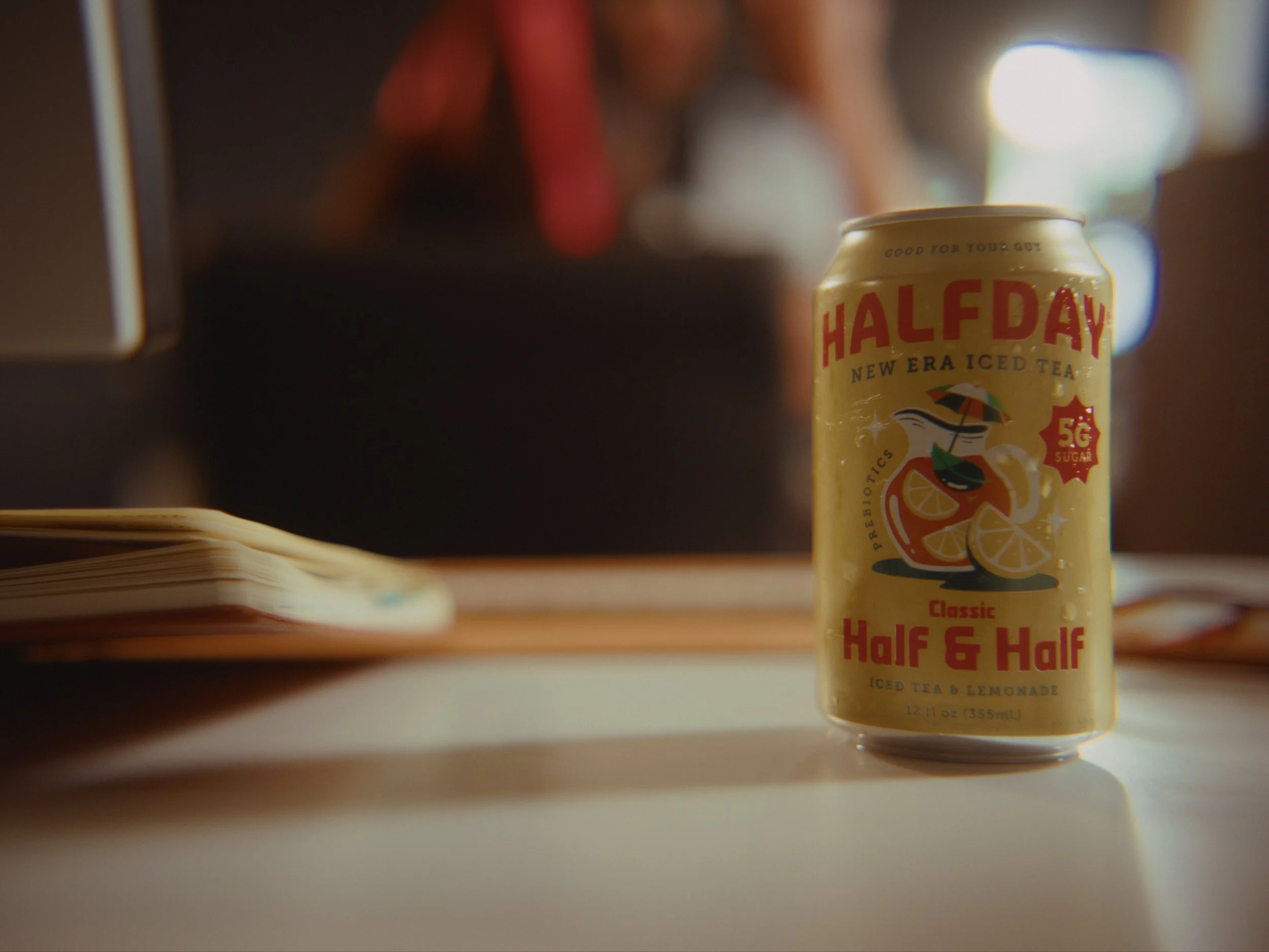 Close-up of a can of Half Day iced tea and lemonade, with a blurred background and an opened book in the foreground.