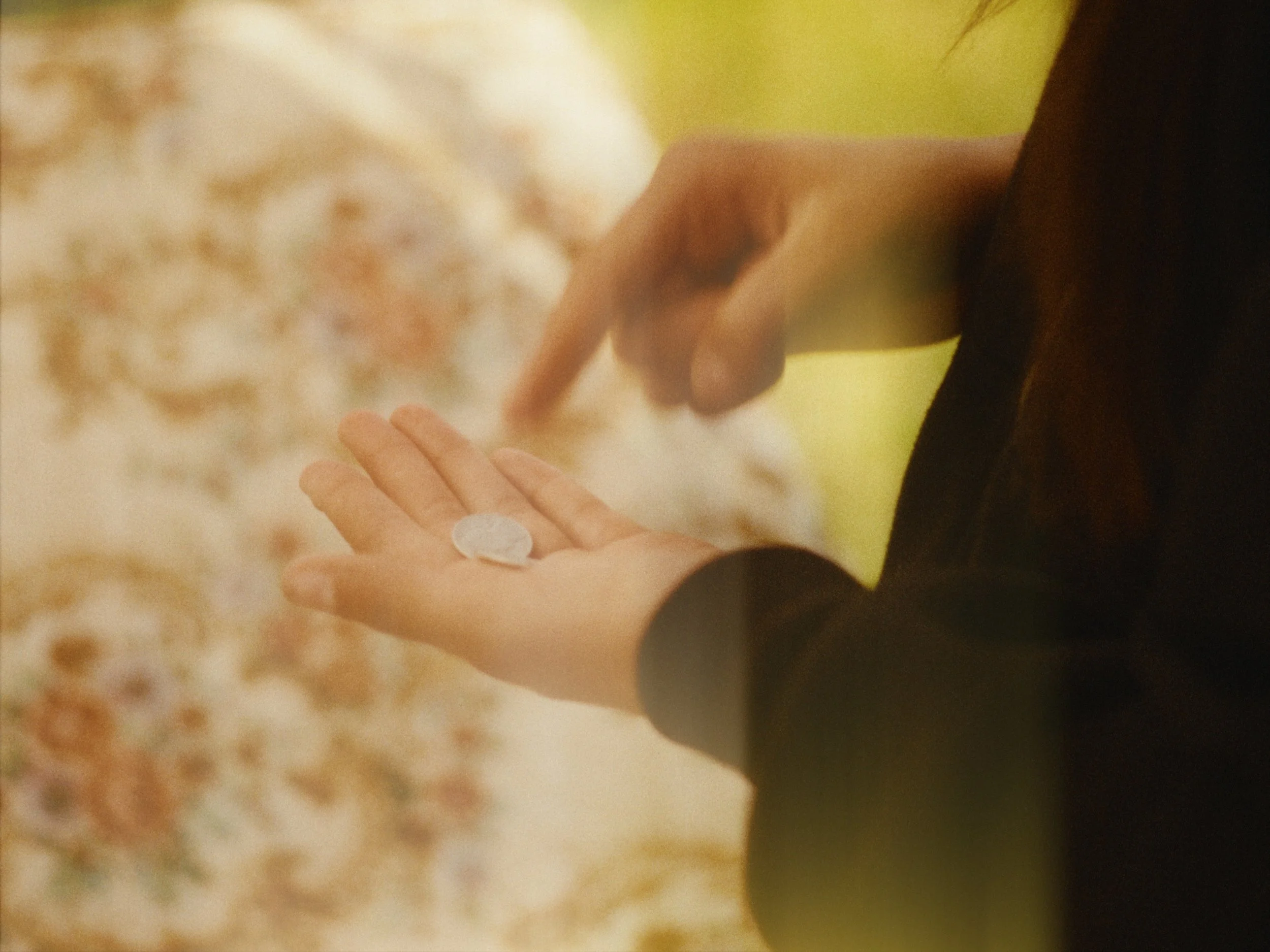 Close-up of a person's hand holding a single white pill, with blurred background.