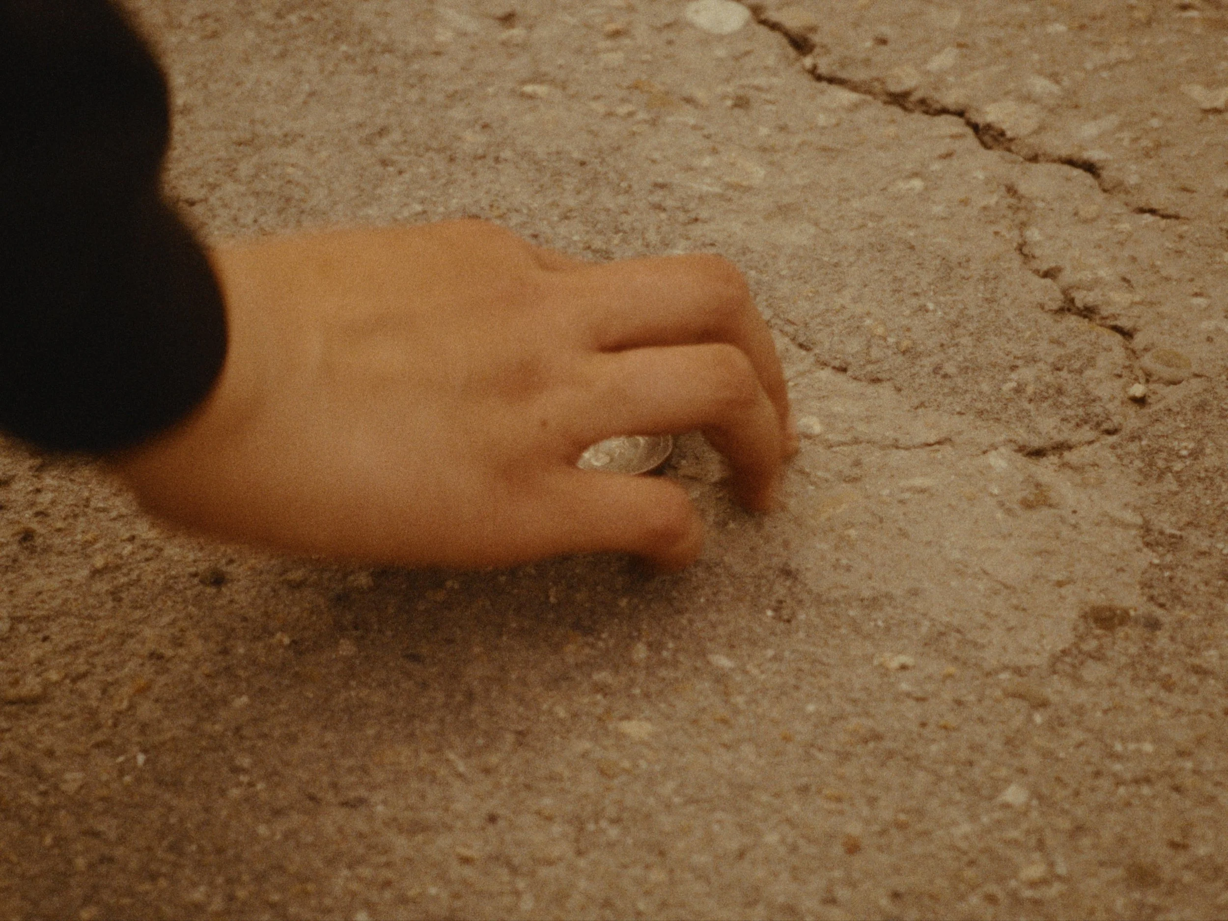 A hand holding a coin close to a cracked, rough concrete surface.
