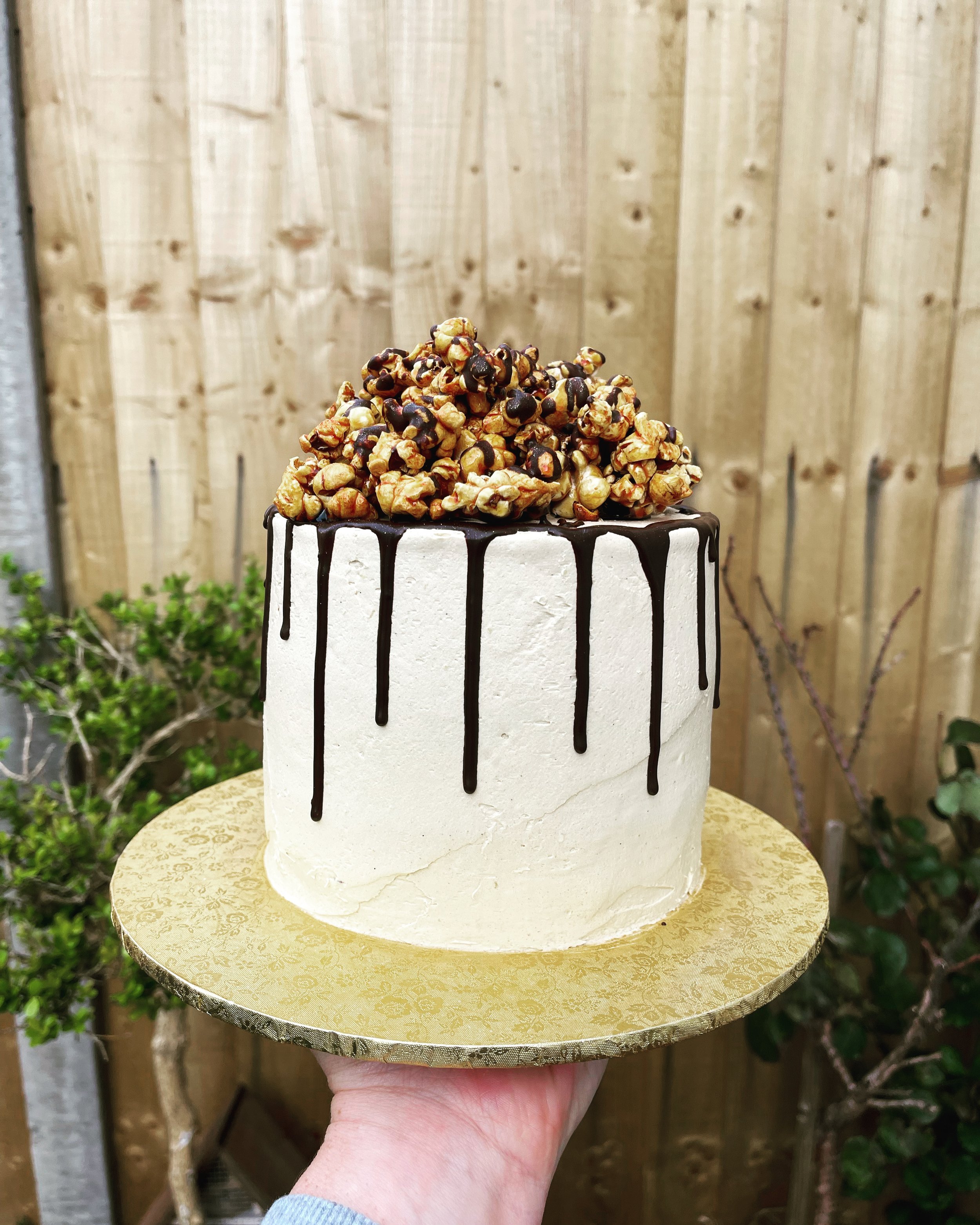 Black and gold two tier with caramel popcorn, macarons, chocolate drip and  custom cake topper