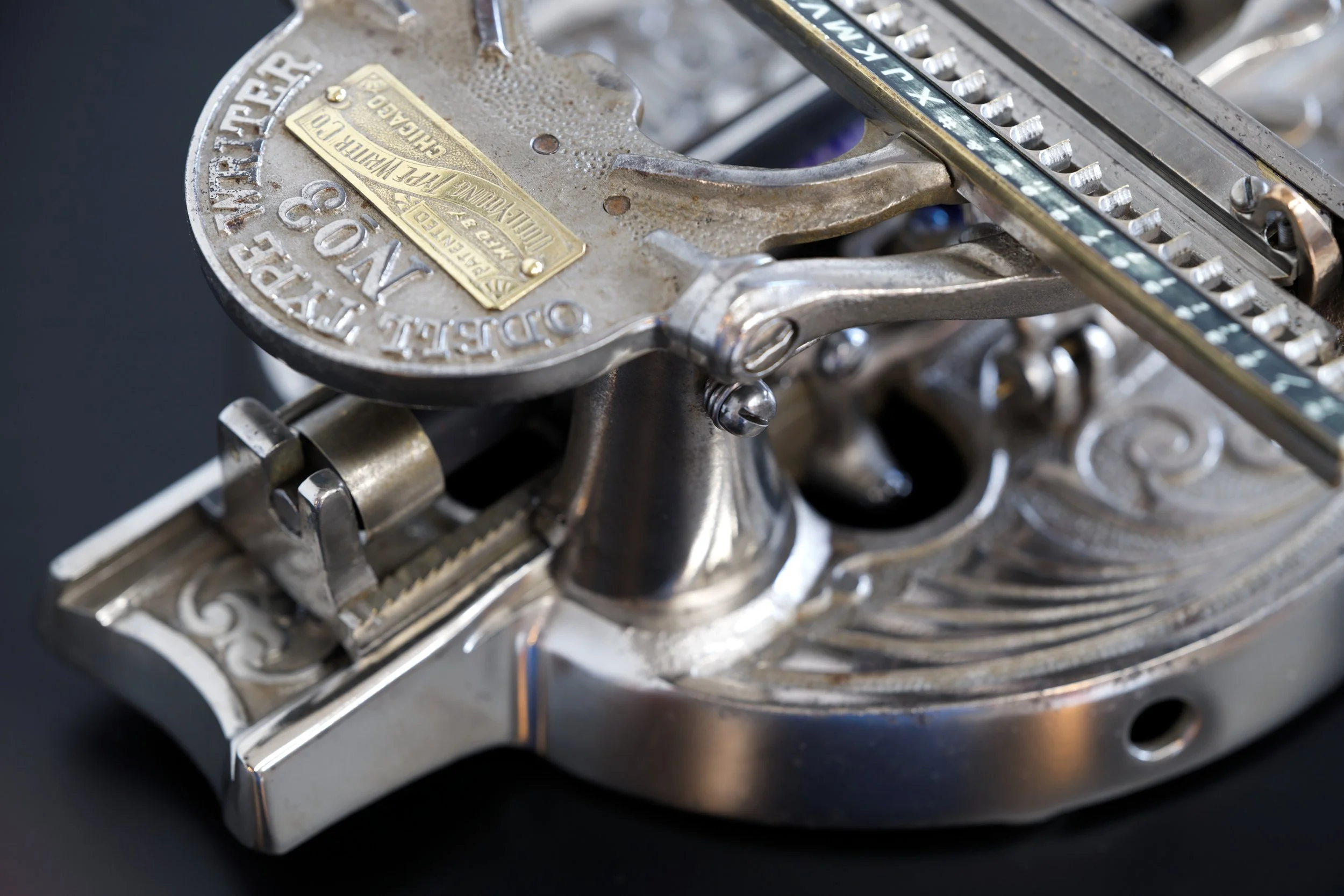 Closeup of the 1890 Odell Model 3 Typewriter showing the brass nameplate and the selection bar