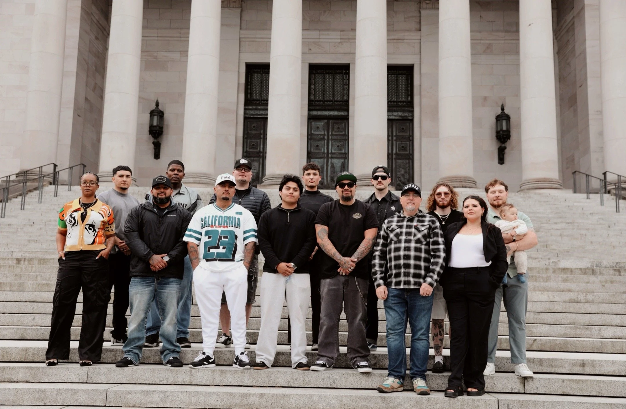 A diverse group of people standing on the steps of a building with large columns and decorative doors, posing for a photo.