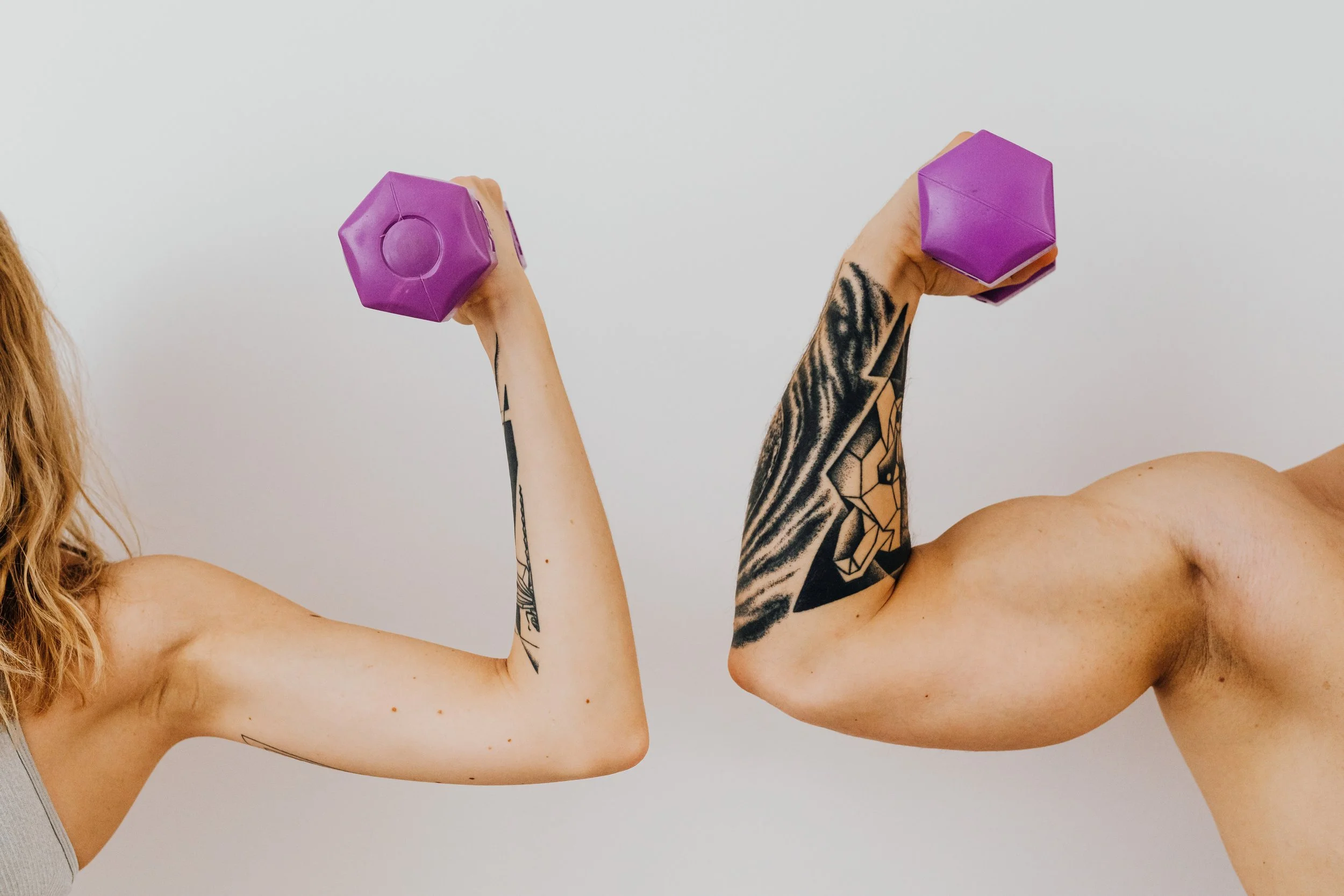 Woman's arm and man's arm with flexed biceps holding small, purple dumbbell