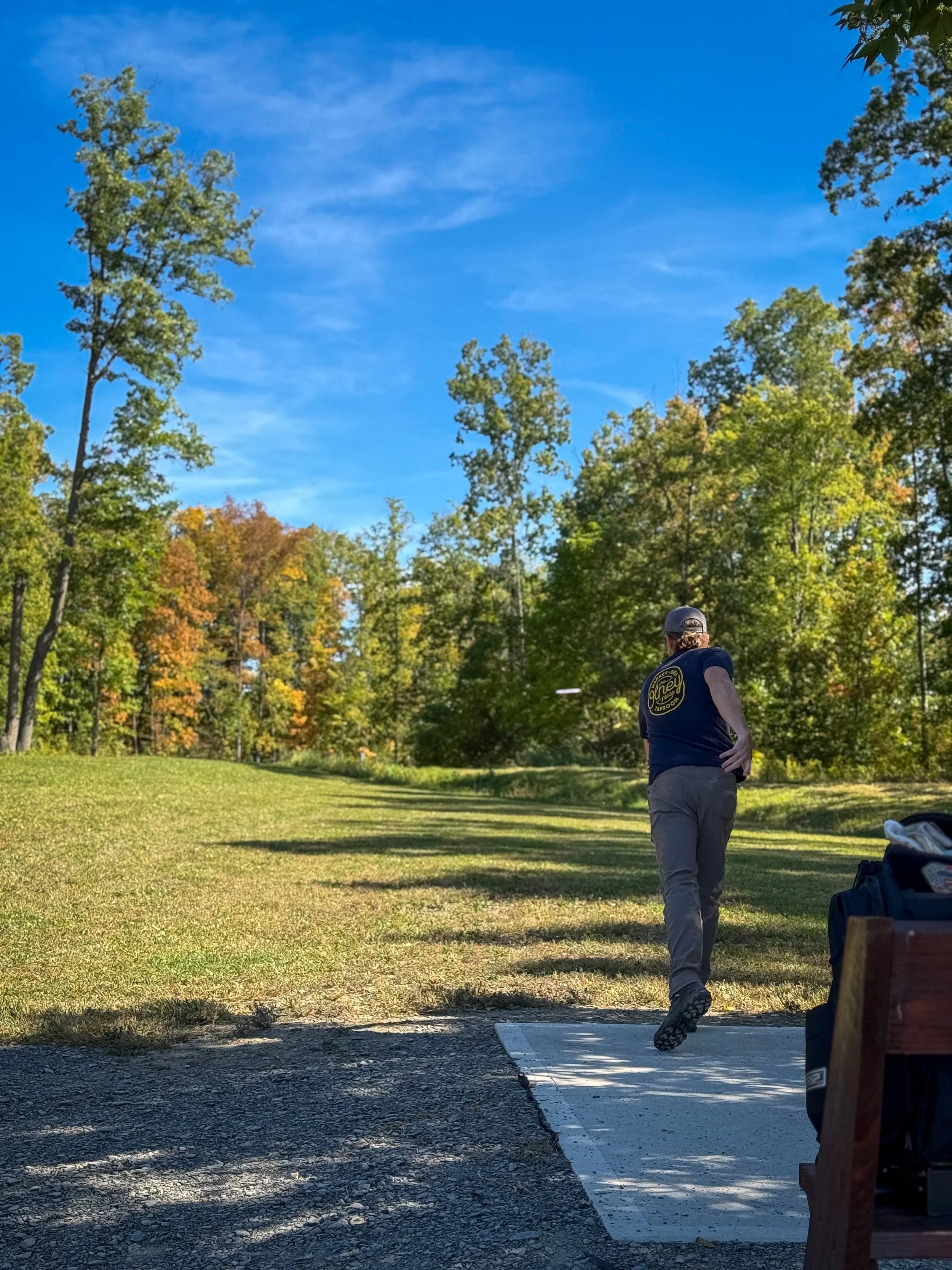 A man playing disc golf on a park course, preparing to throw a disc with trees and a blue sky in the background.