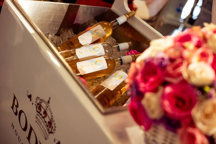 Four bottles of rosé wine in a silver ice cooler, with a blurred bouquet of pink and cream roses nearby.